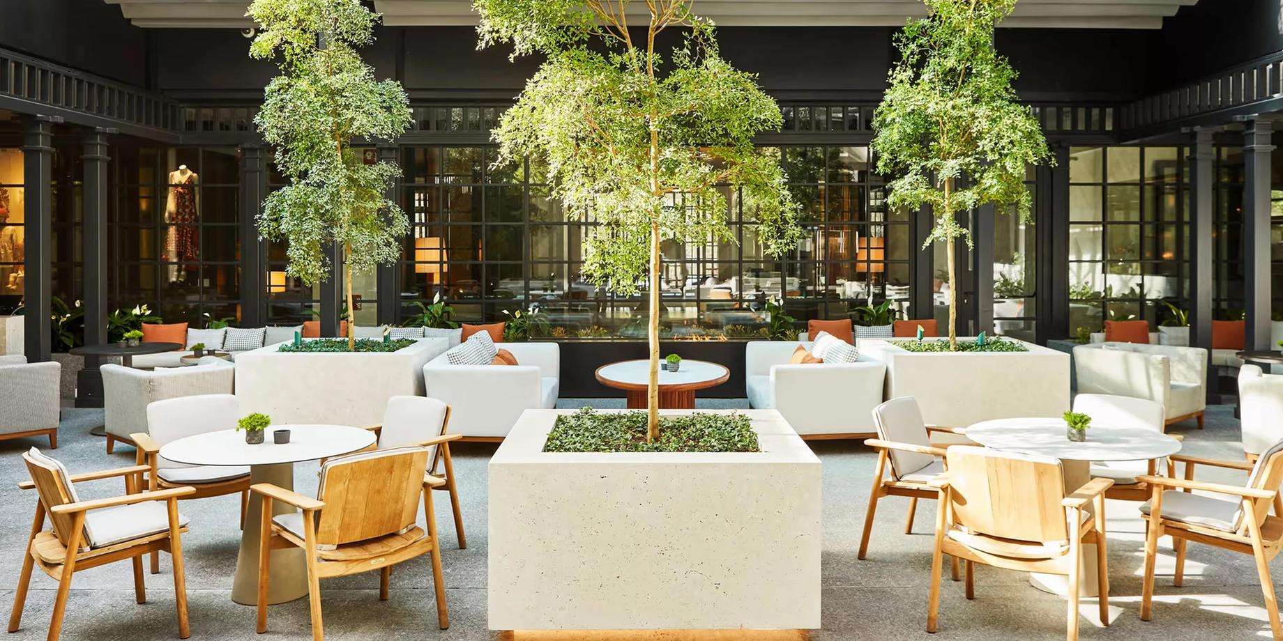 The hotel courtyard with lush trees, white seating, and columned architecture in Madrid