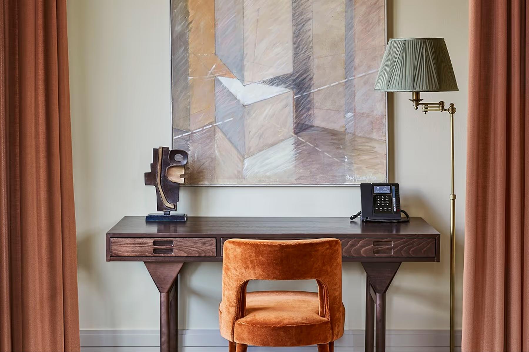 De L’Europe Amsterdam: workspace area with wooden desk, striped upholstered chair, and abstract artwork