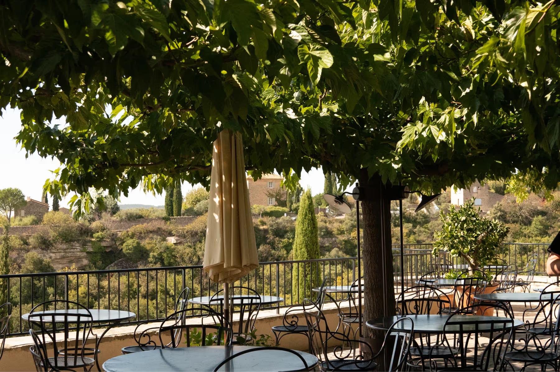 Airelles Gordes, La Bastide: terrace dining under grapevine canopy with valley and church views