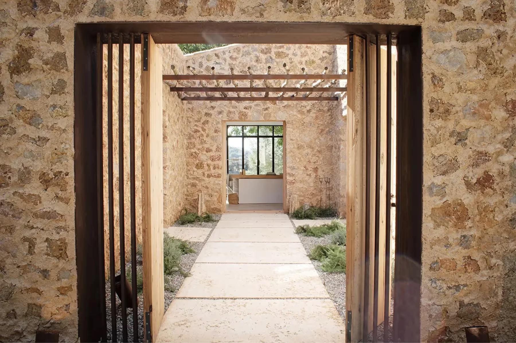 Es Racó d’Artà: passageway through stone walls with wooden doors and natural light spilling across floor