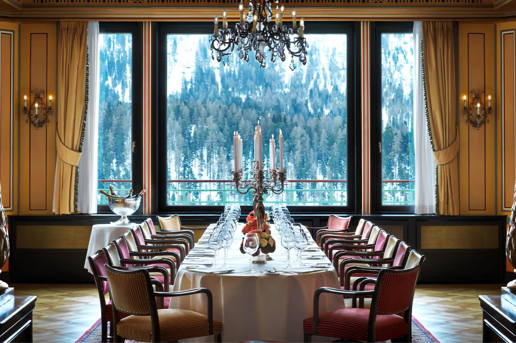 Long dining table with burgundy chairs, wood paneling, and alpine mountain views
