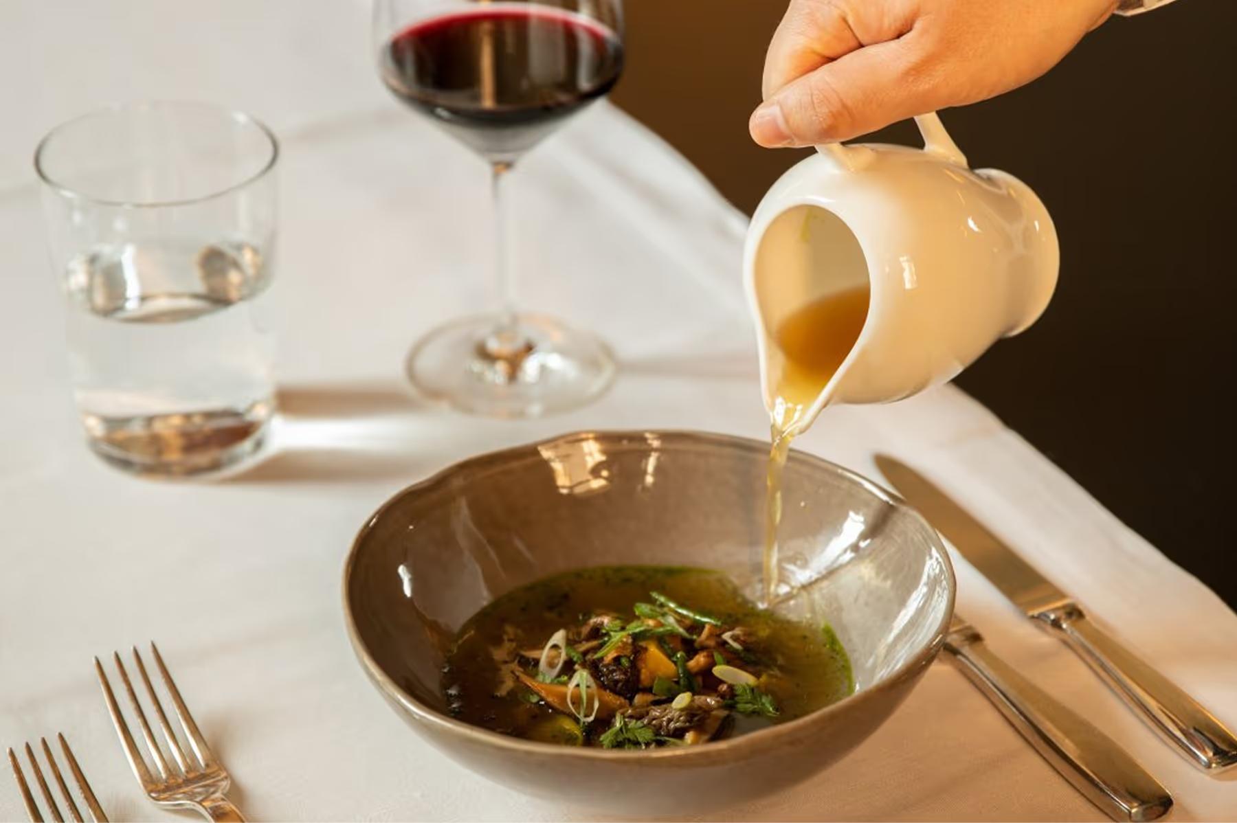Aman Venice: a plated dish of pasta with sauce and garnish being served at a table with wine and glassware
