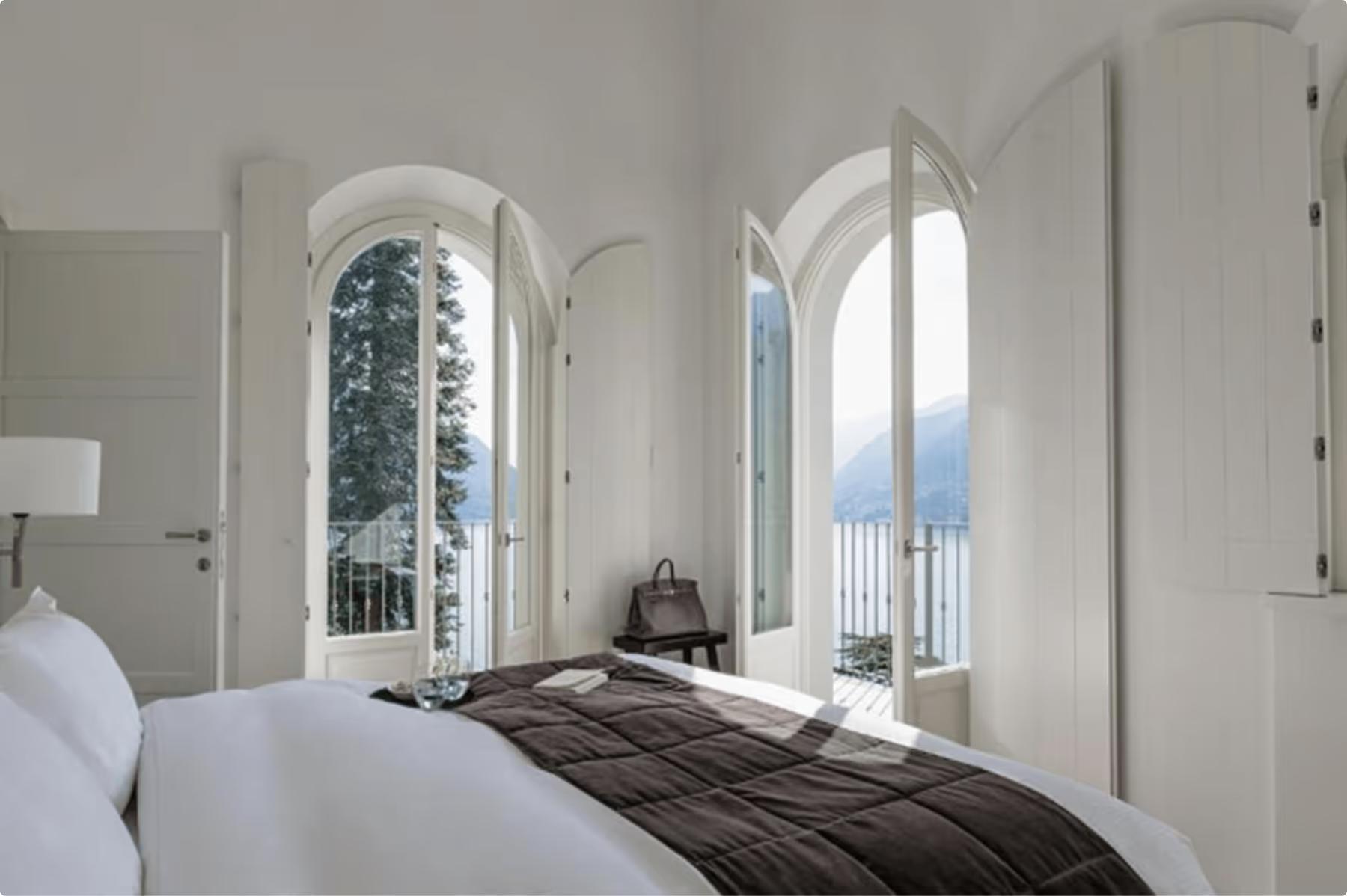 Villa Làrio: bedroom with arched windows overlooking the lake and pale bedding with dark accent