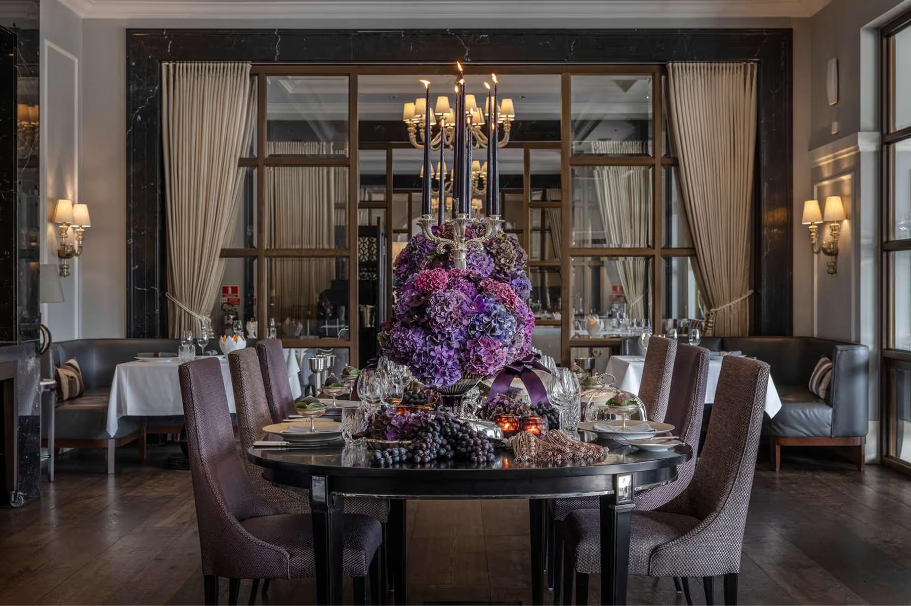 Round dining table with purple floral centerpiece and dark furnishings