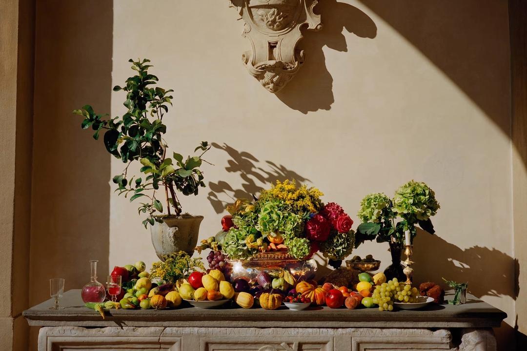 A still life of Tuscan fruit, vegetables and flowers arranged along a carved stone console in raking light
