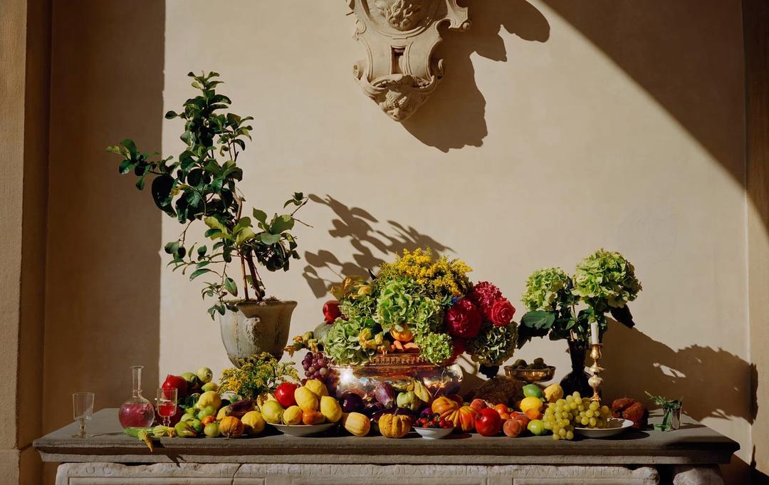 A still life of Tuscan fruit, vegetables and flowers arranged along a carved stone console in raking light