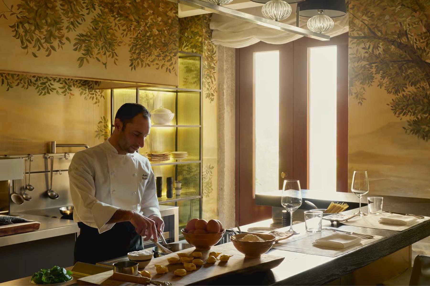 Aman Venice: an open kitchen with a chef preparing pasta, warm lighting overhead, and ceramic bowls of ingredients nearby