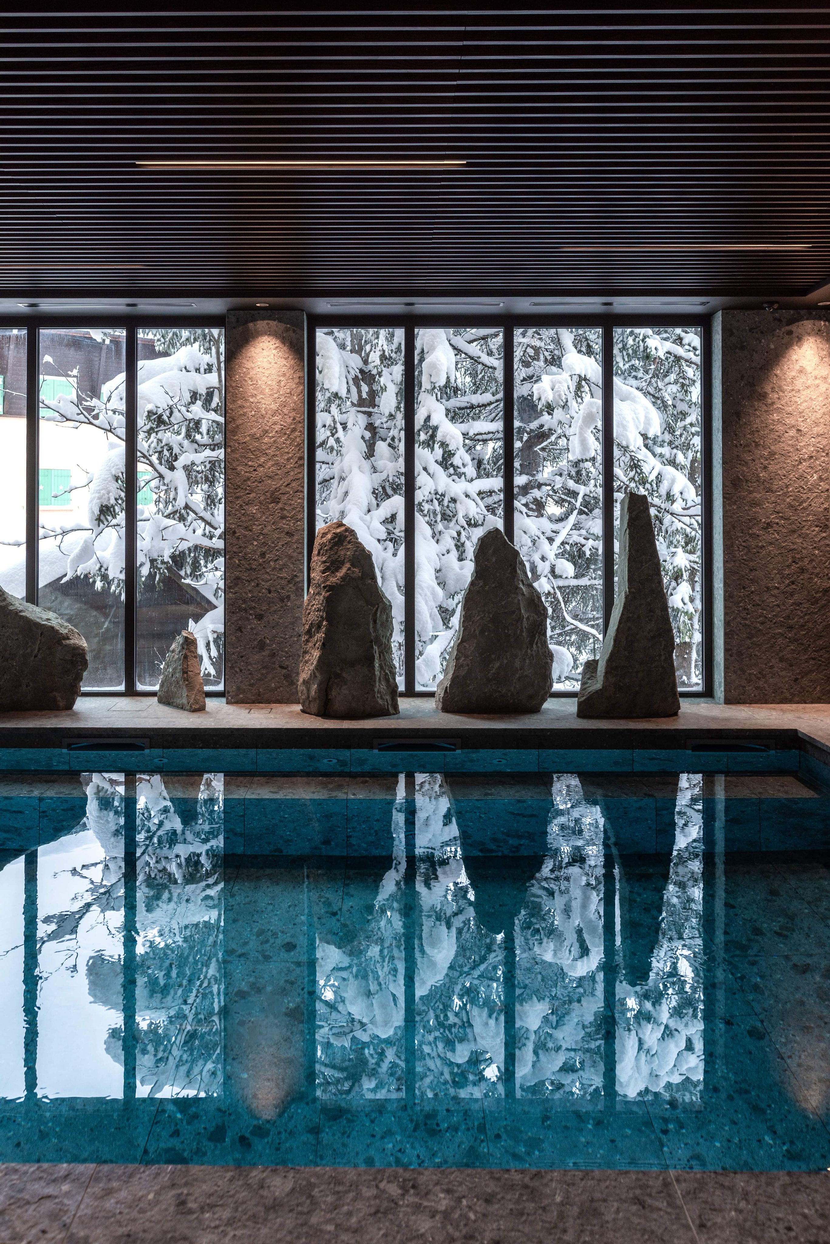 An indoor pool with standing stones against windows of snowy forest in Megève