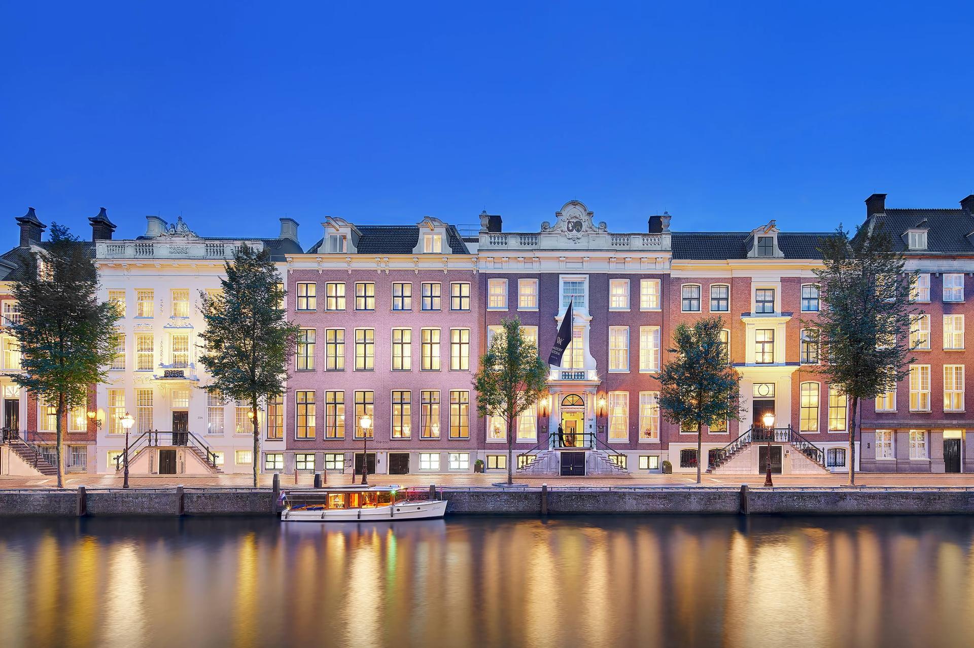 Waldorf Astoria Amsterdam: illuminated historic facades reflected in the canal at dusk, brick palaces with gabled roofs and shuttered windows
