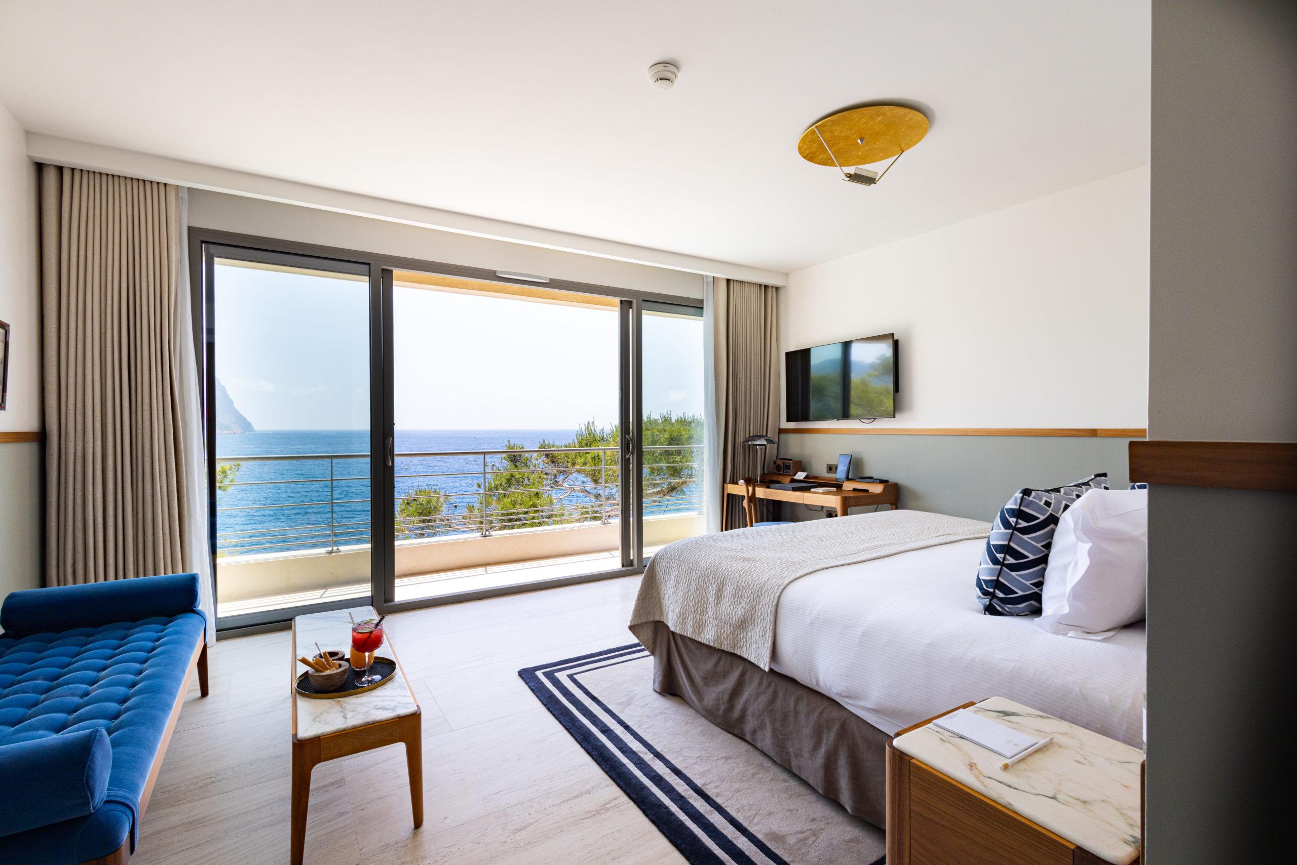 Les Roches Blanches: a bedroom with queen bed, floor-to-ceiling windows framing coastal views, and minimal decor