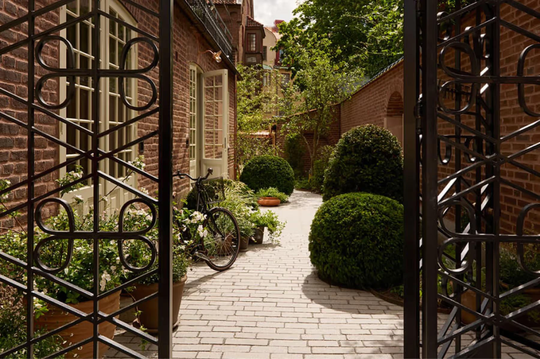 Ett Hem: a garden pathway with ironwork gates, planted borders, and brick paving
