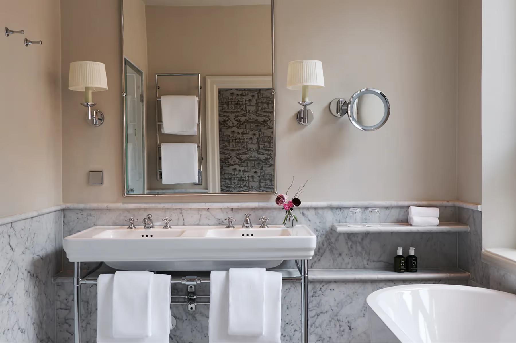 Bathroom with marble counter, dual sink, and circular mirror above vanity