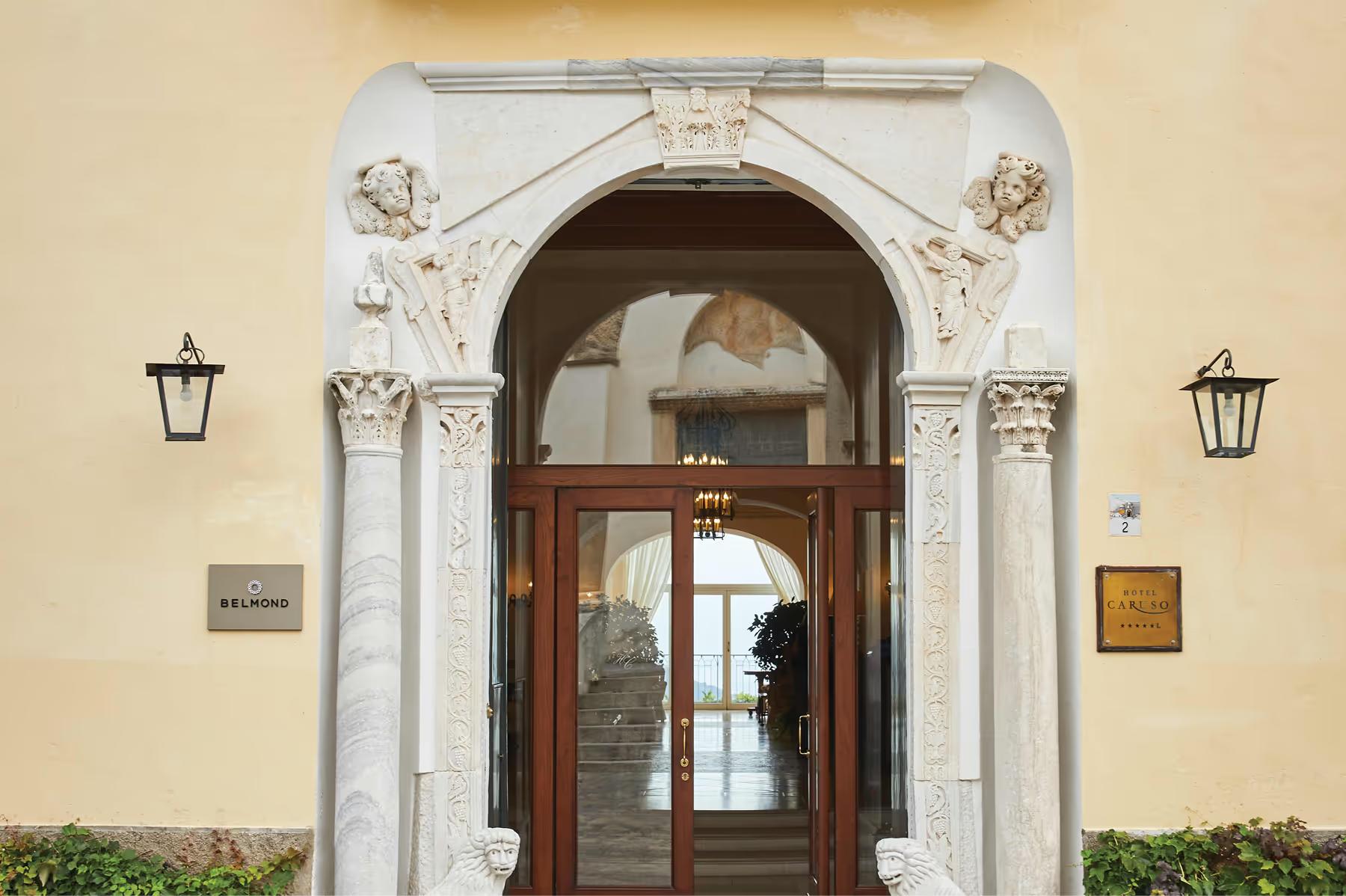 Ornate arched doorway with carved stone columns, dark wood doors, and brass fixtures on cream facade