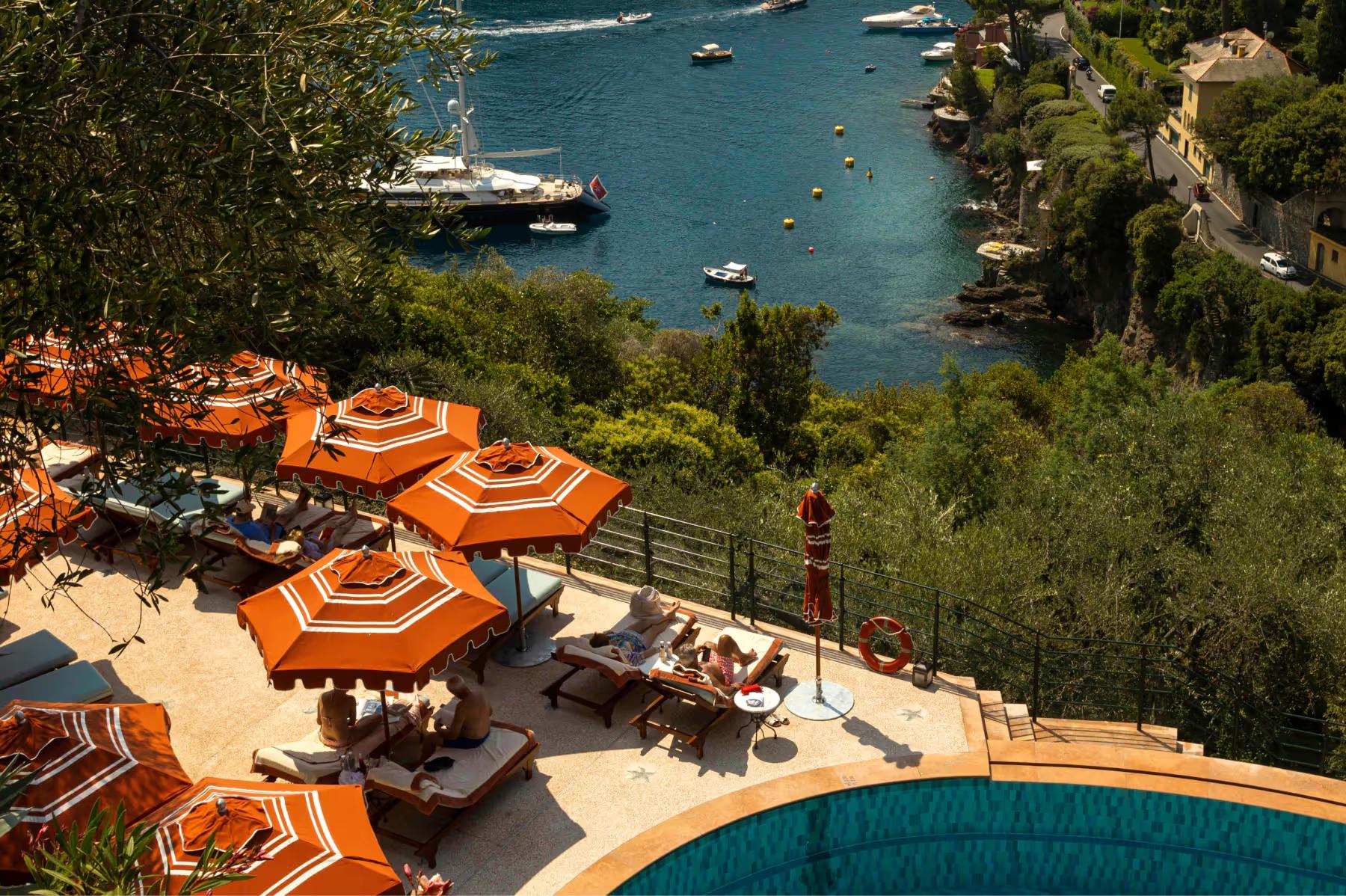Splendido: bright orange umbrellas and sunbeds on a terraced beach platform above the cove