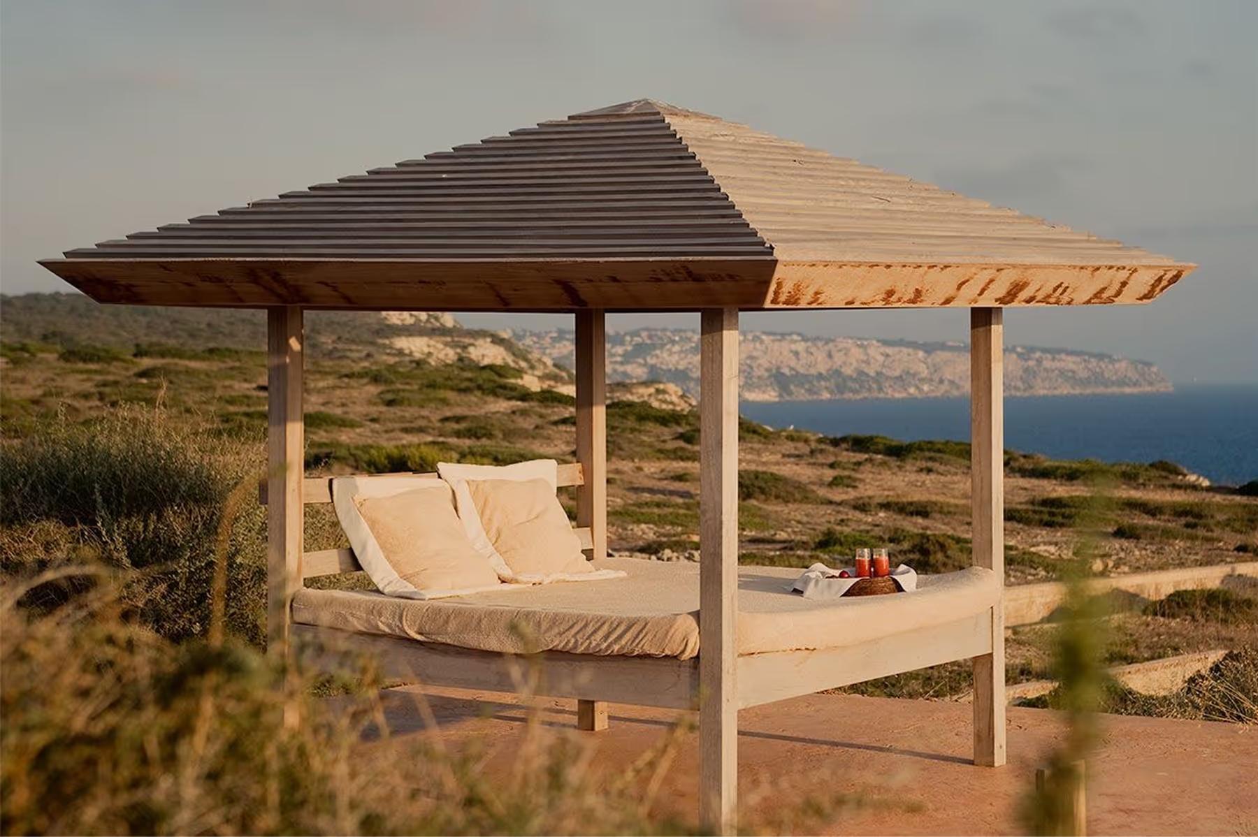 Cap Rocat: a bed with pale curtains and wooden ceiling, framed by an open terrace and coastal light