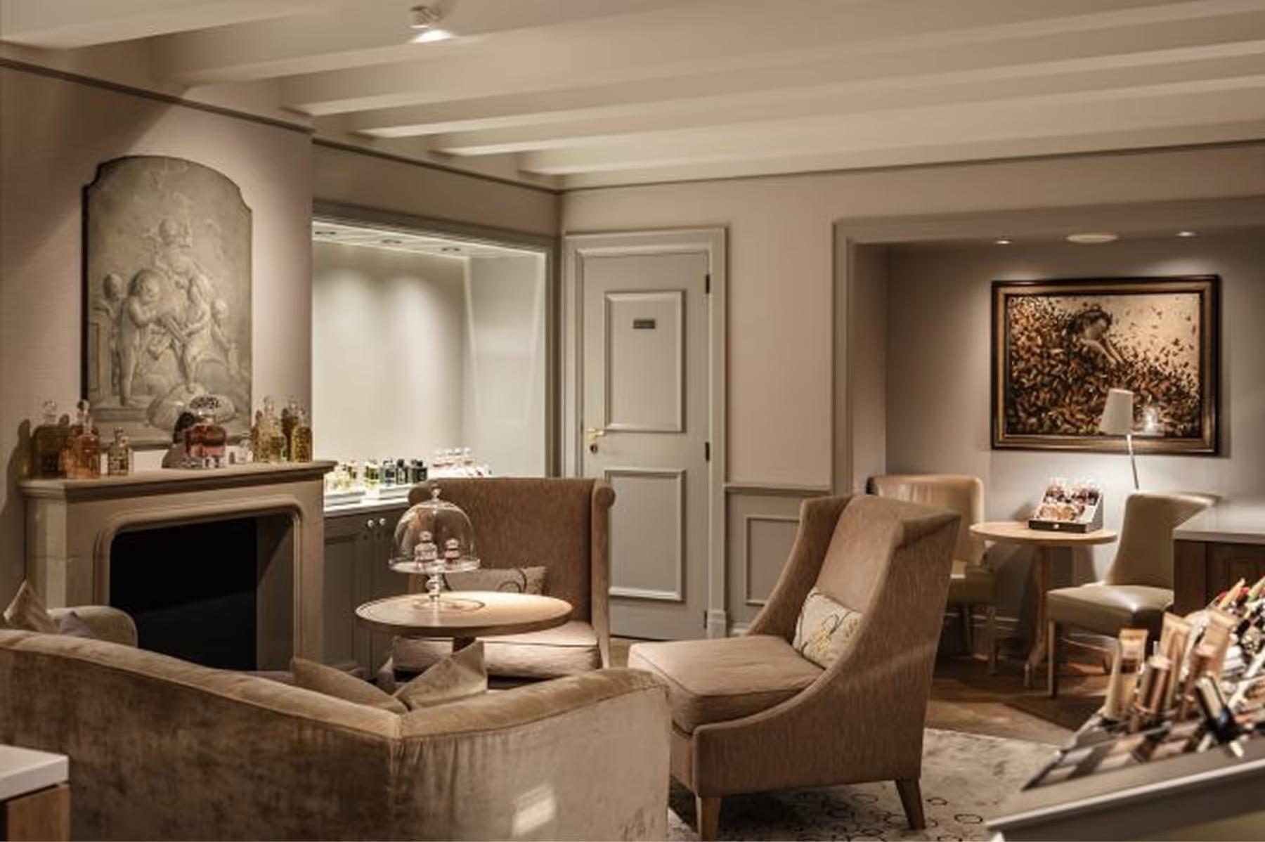 A spa lounge with cream armchairs, a marble fireplace surround, and framed botanical artworks