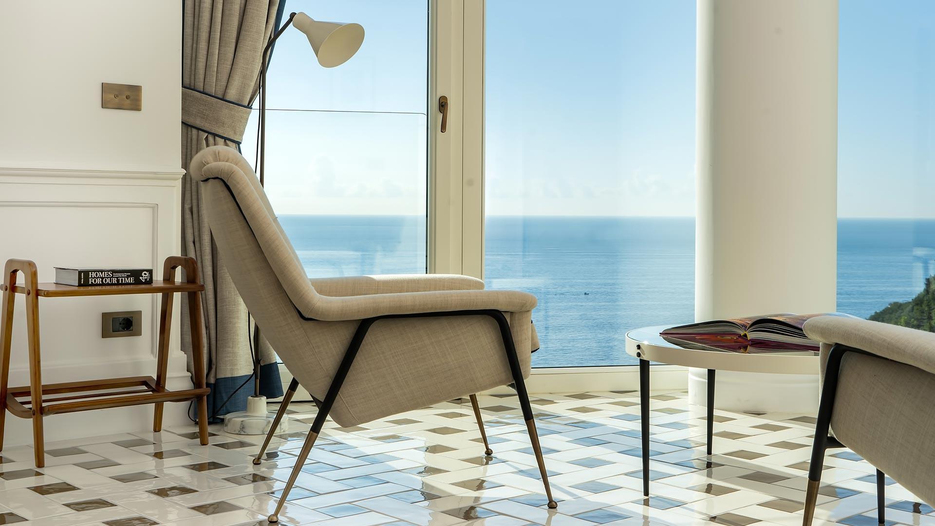Borgo Santandrea: minimalist seating area with modern chair overlooking seascape through floor-to-ceiling windows