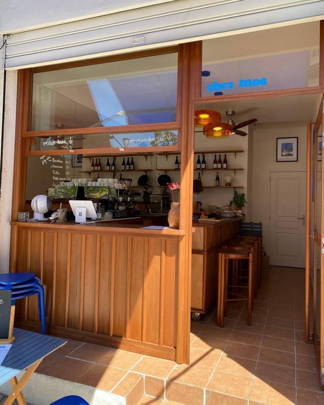 The open counter at Chez Moe, with a blue neon sign, shelves of wine, and wooden bar stools