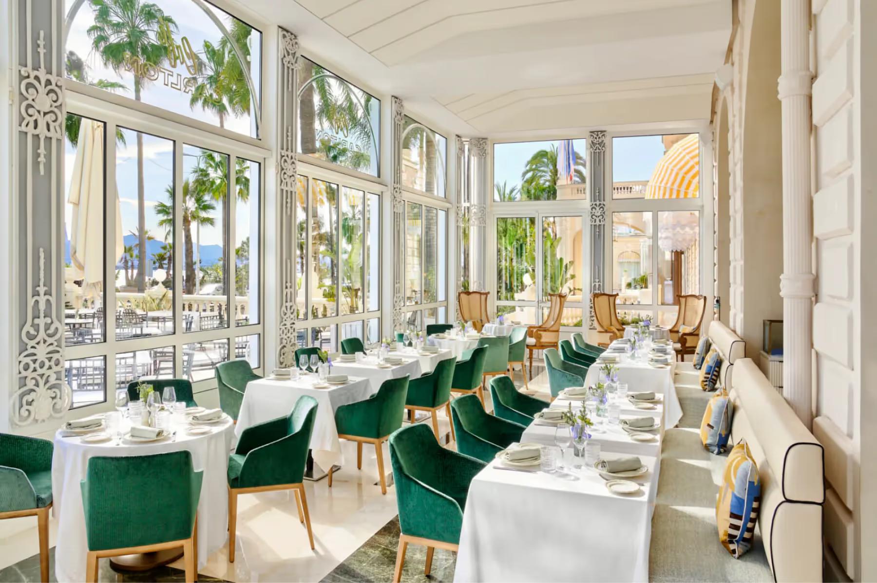Carlton Cannes: fine dining room with windows, white tablecloths, green velvet chairs, and ornate ceiling detail