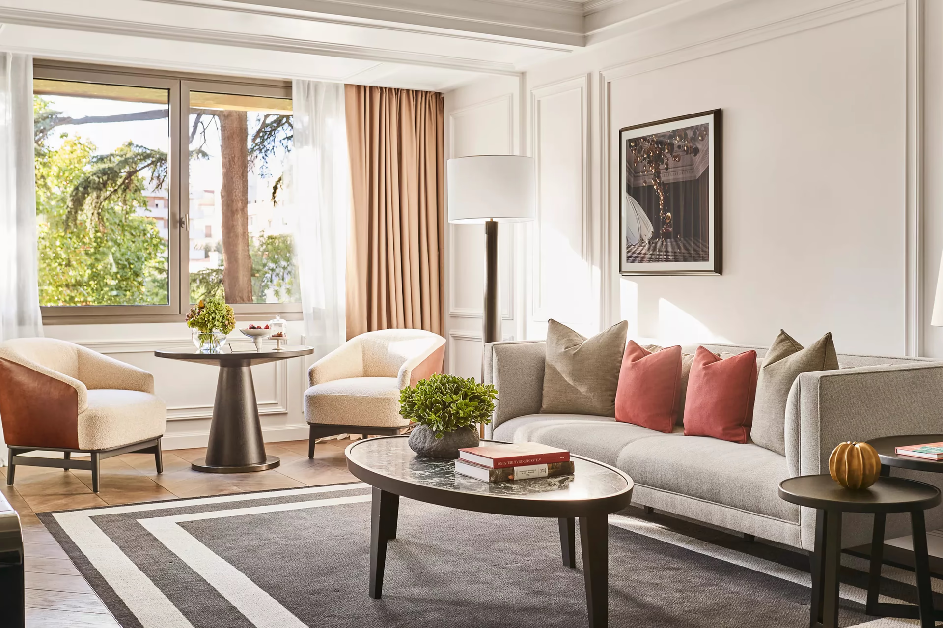 Rosewood Villa Magna: a living room with gray upholstered sofa, gold chandelier, and large windows overlooking the city