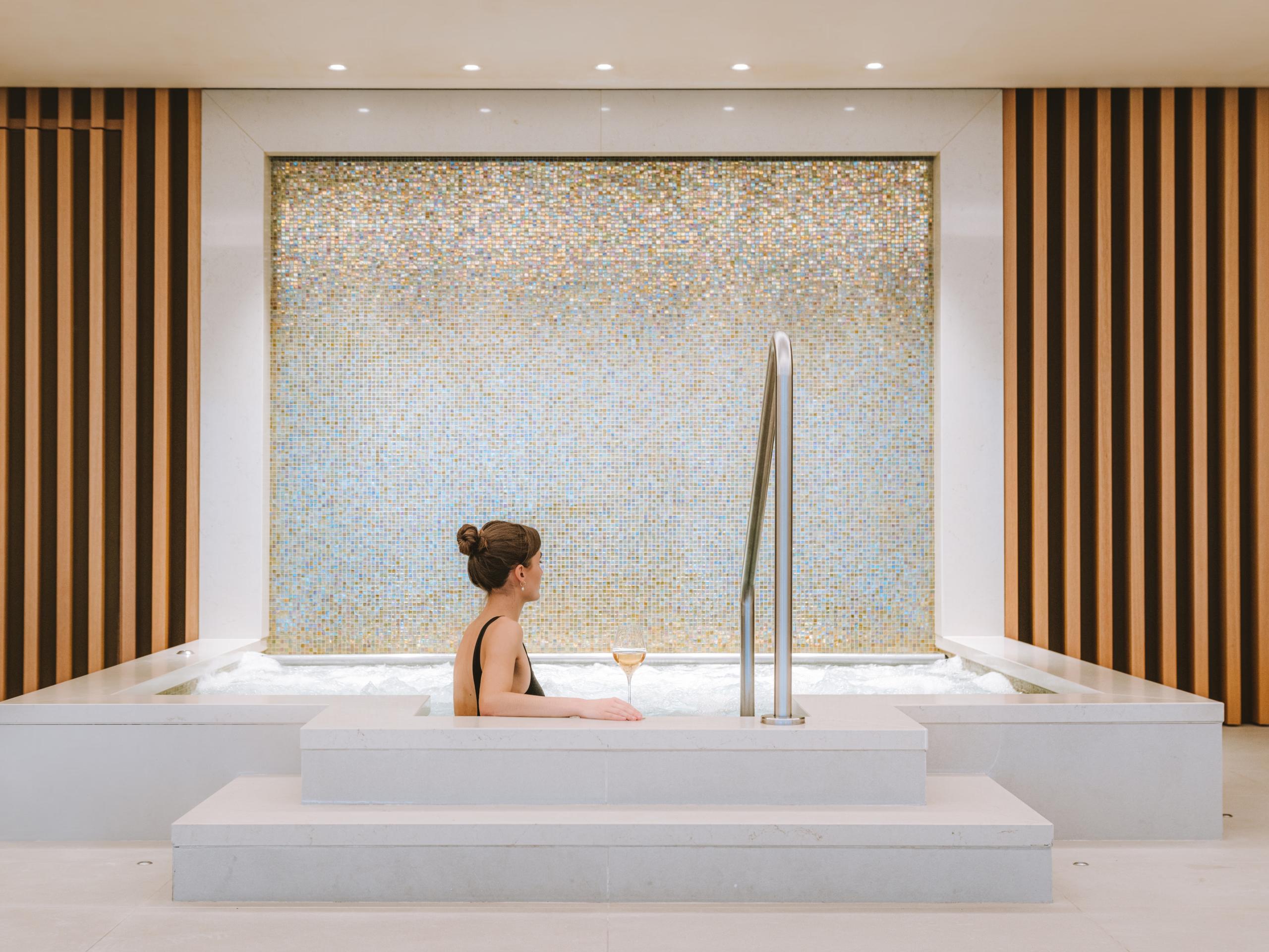 Woman in spa tub with marble mosaic backdrop and vertical wood slat detailing
