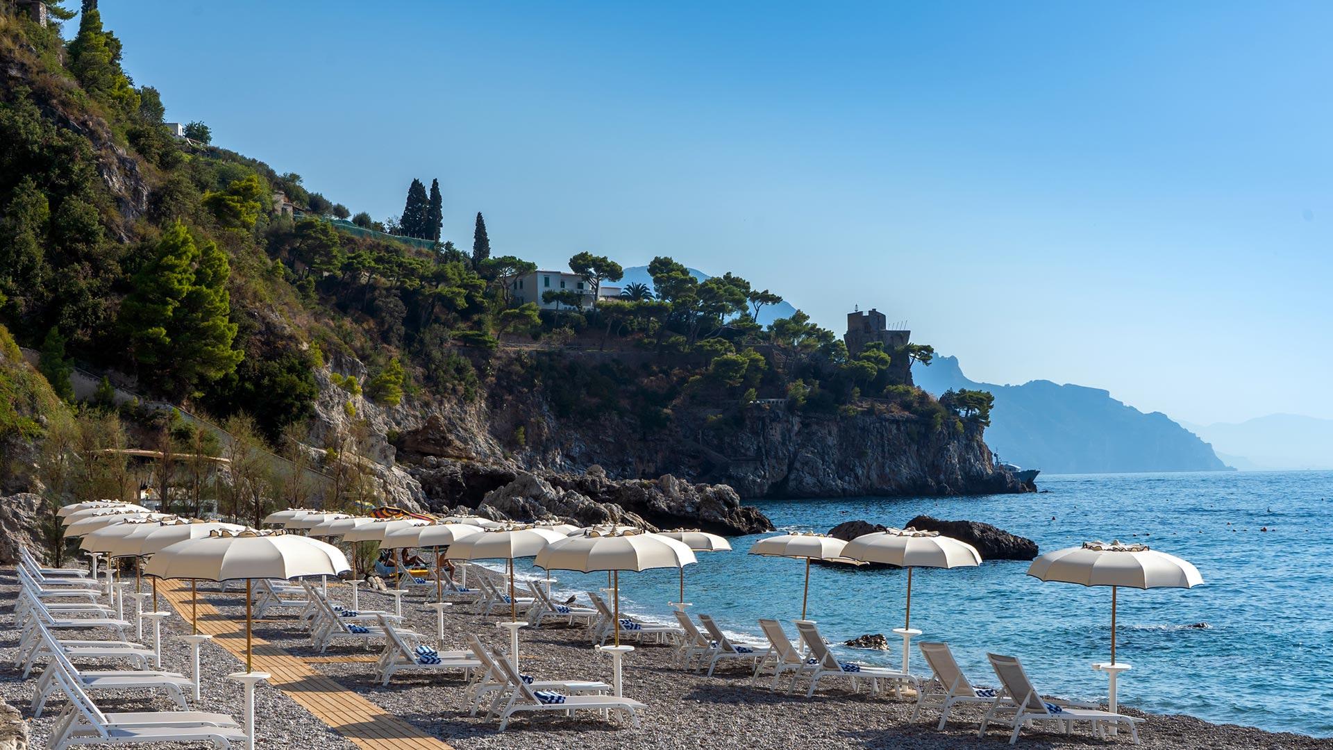 Borgo Santandrea: private beach club with loungers and parasols on pebble shore below cliffs