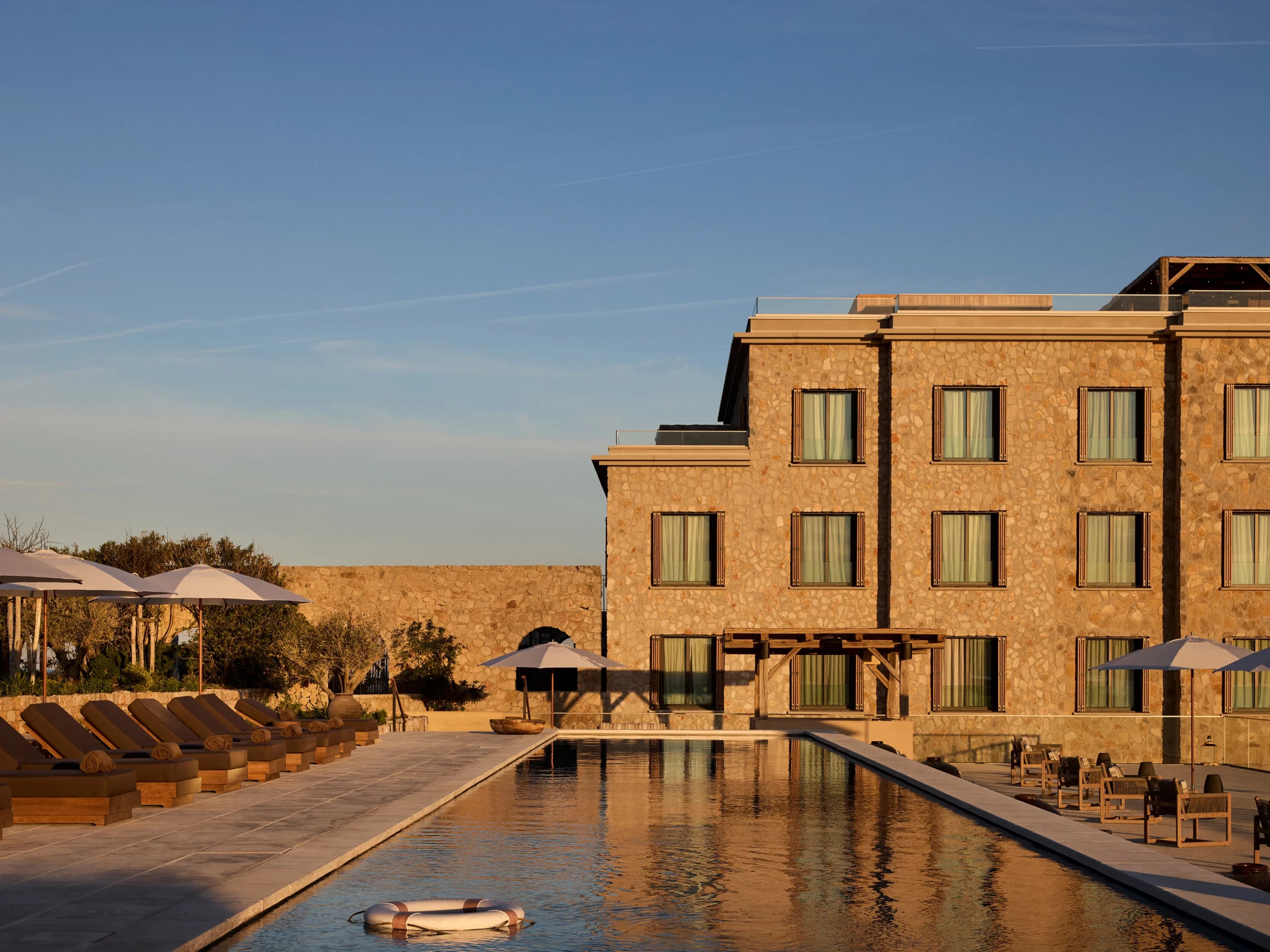Zannier Île de Bendor: morning light warms the stone hotel wing above a reflecting pool lined with white parasols