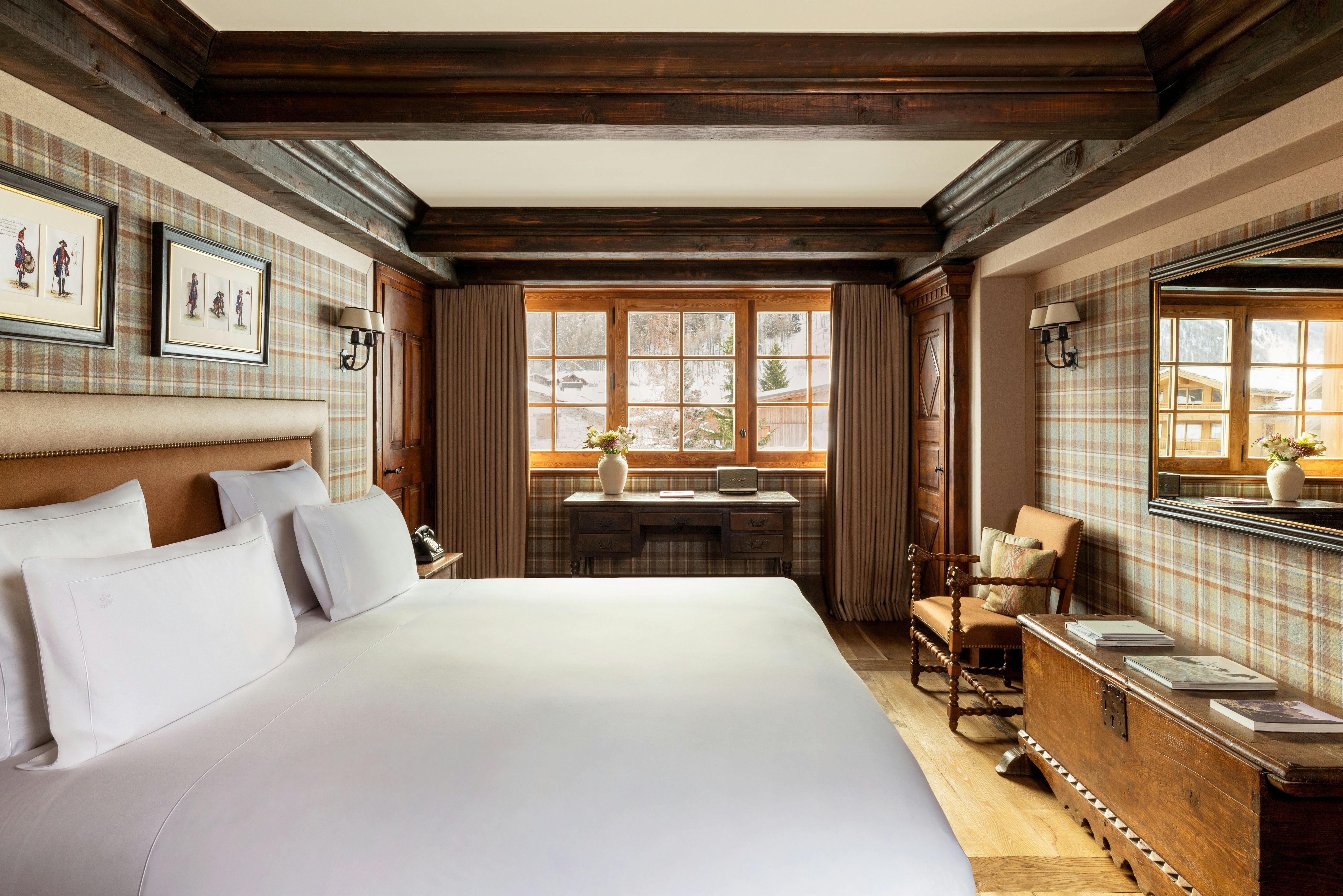 A bedroom at Airelles Val d’Isère with dark beams, tartan walls, and a bright window