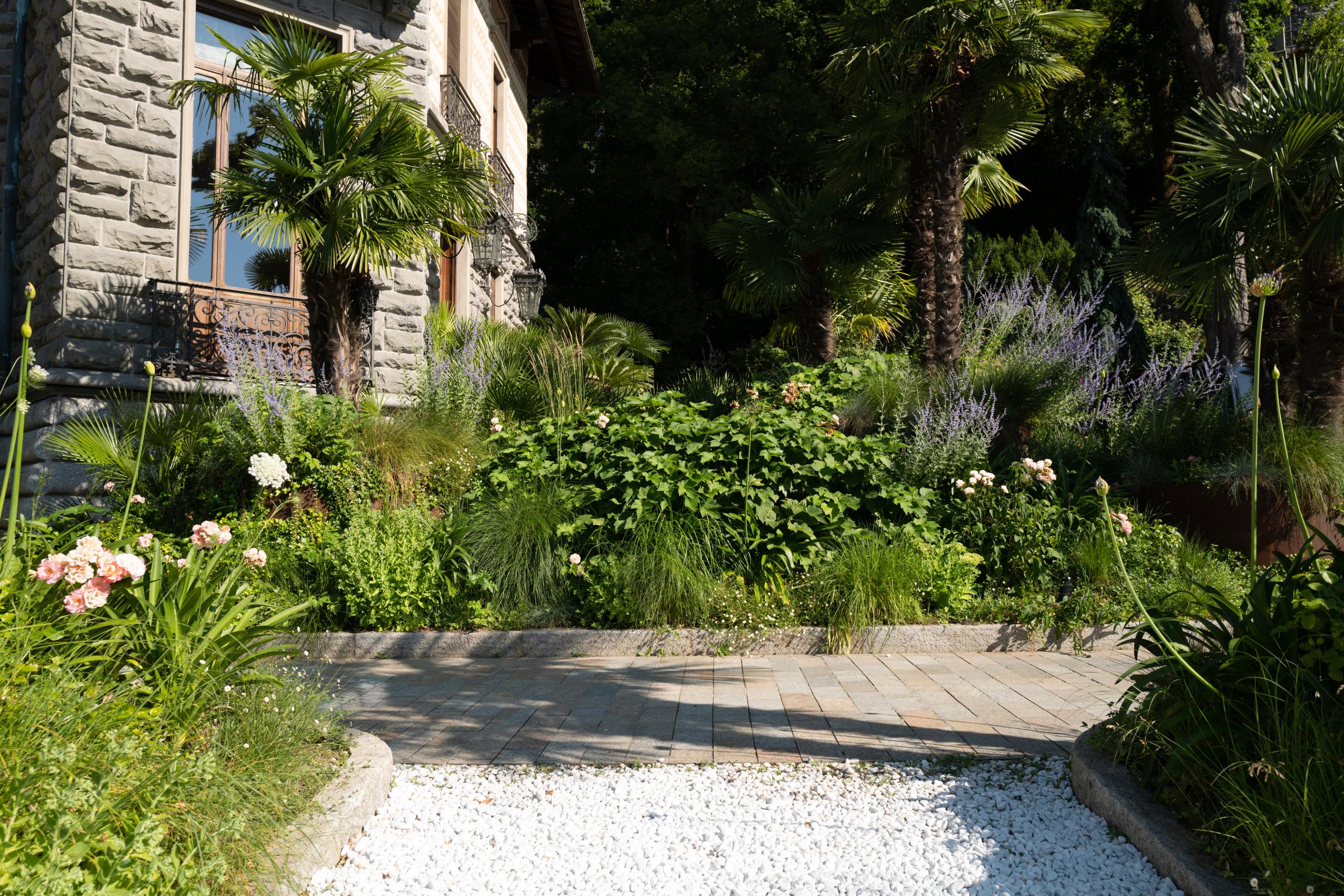 Shaded garden path with potted plants, flowering vines, and stone architecture