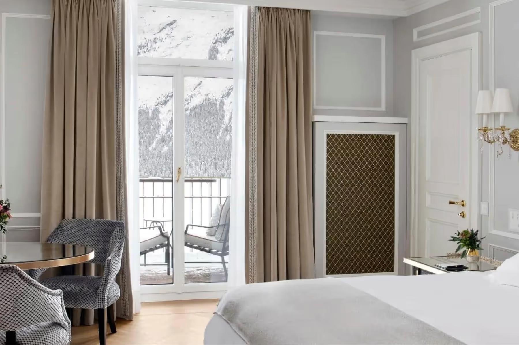 Badrutt’s Palace Hotel: bedroom with cream-colored walls, tall windows with valley views, tan curtains