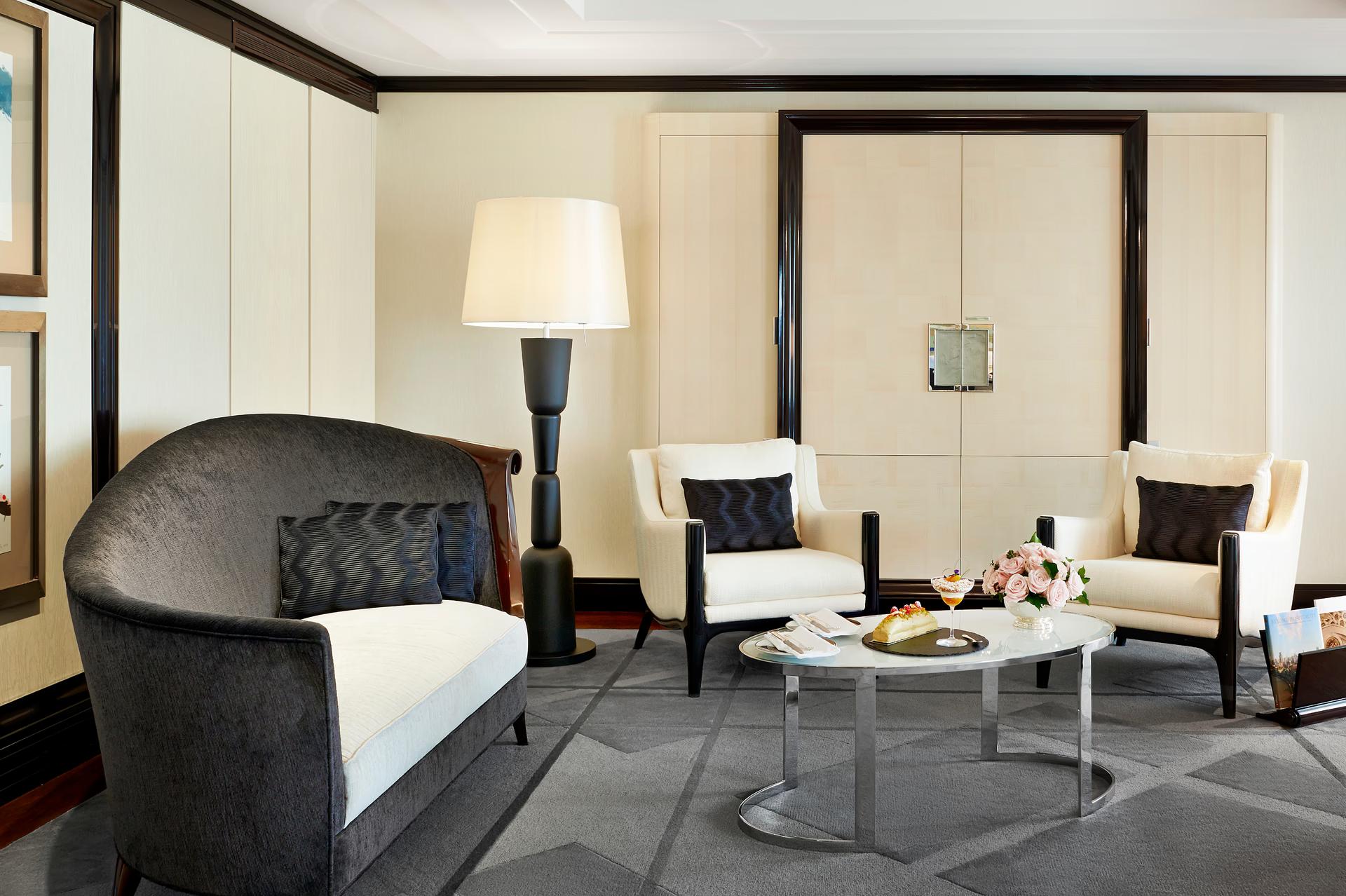 The Peninsula: suite sitting area with curved charcoal loveseat, cream chairs, and warm ambient lighting