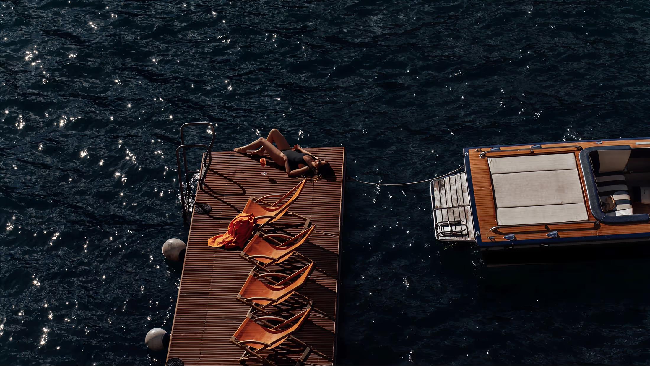 Wooden sunloungers with golden rope detail on a dark water surface