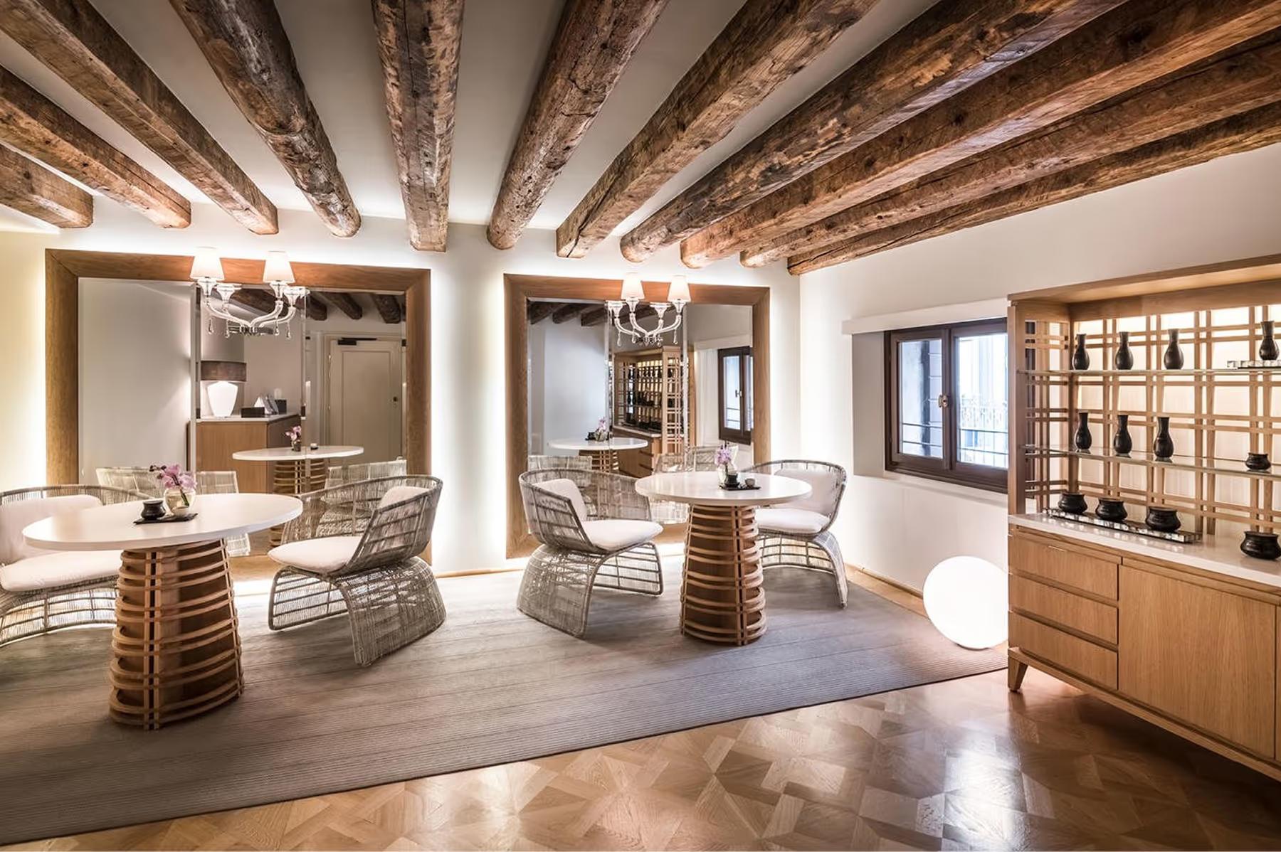A yoga studio with wooden beams, natural light, cream furnishings, and floor cushions