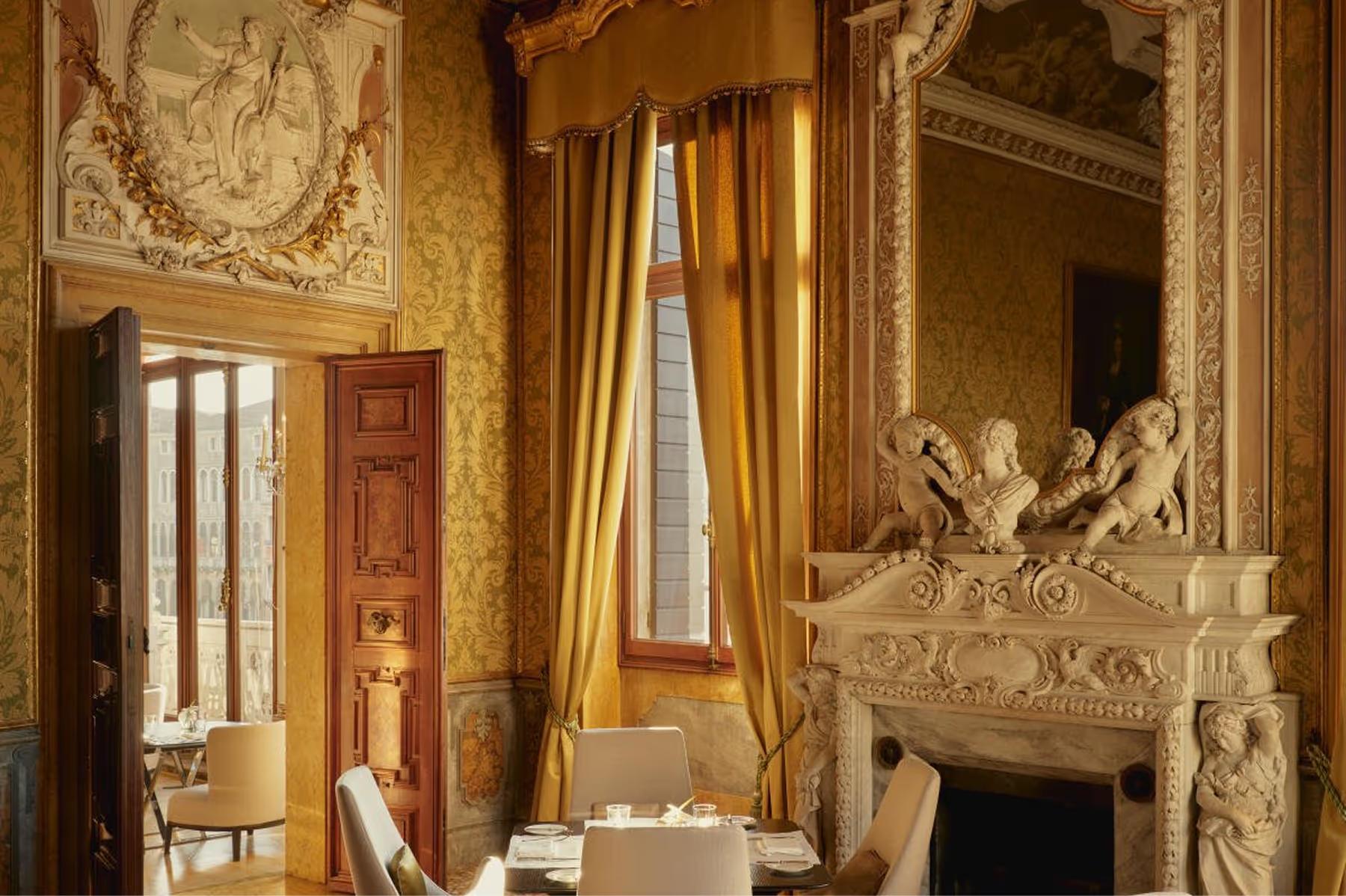 A corridor with mustard-colored walls, ornate gold-framed mirror, and sculptural white plaster details above doorways