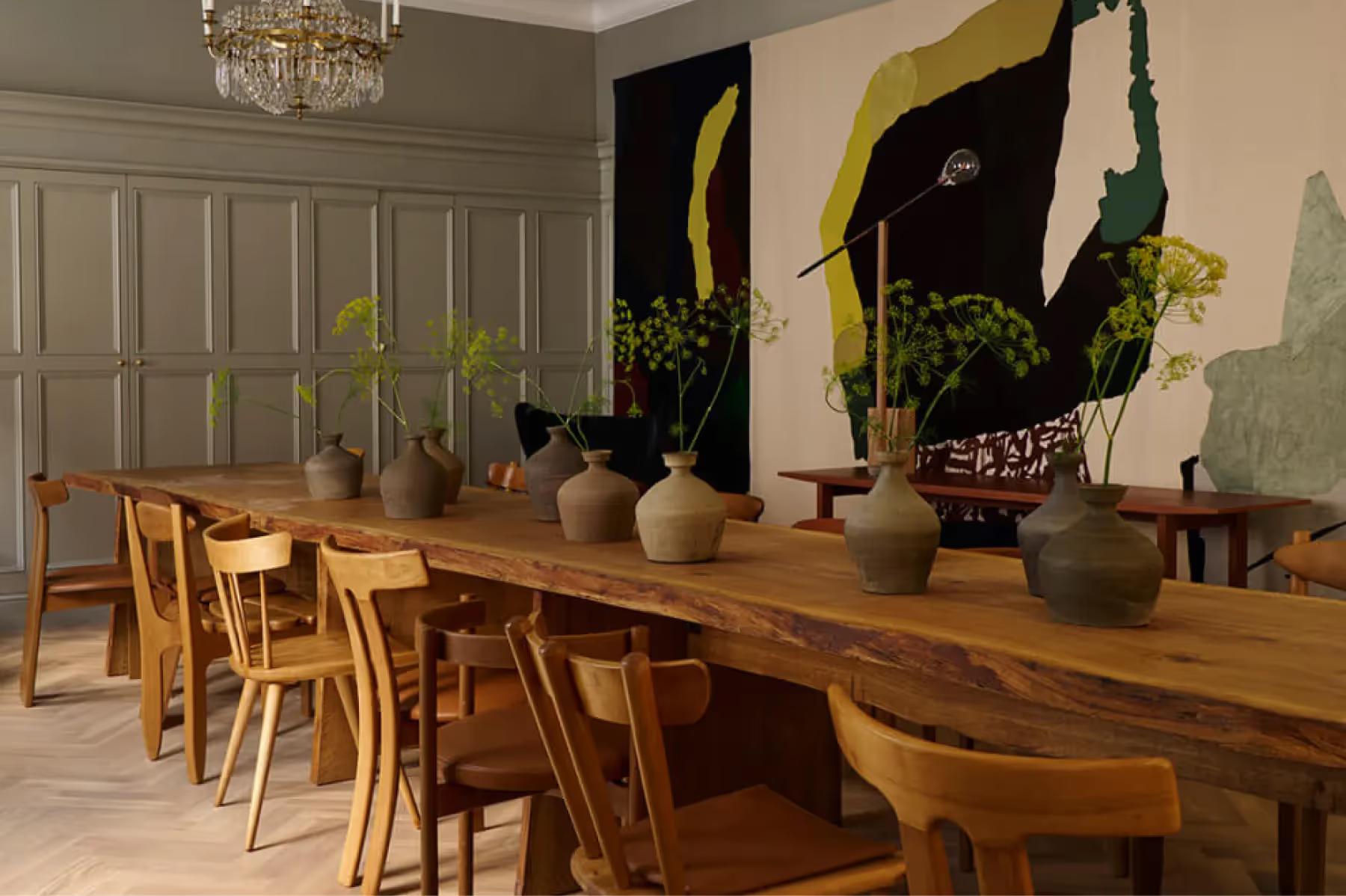 Ett Hem: a dining room with wooden table and chairs, potted plants, and dark artwork on neutral walls