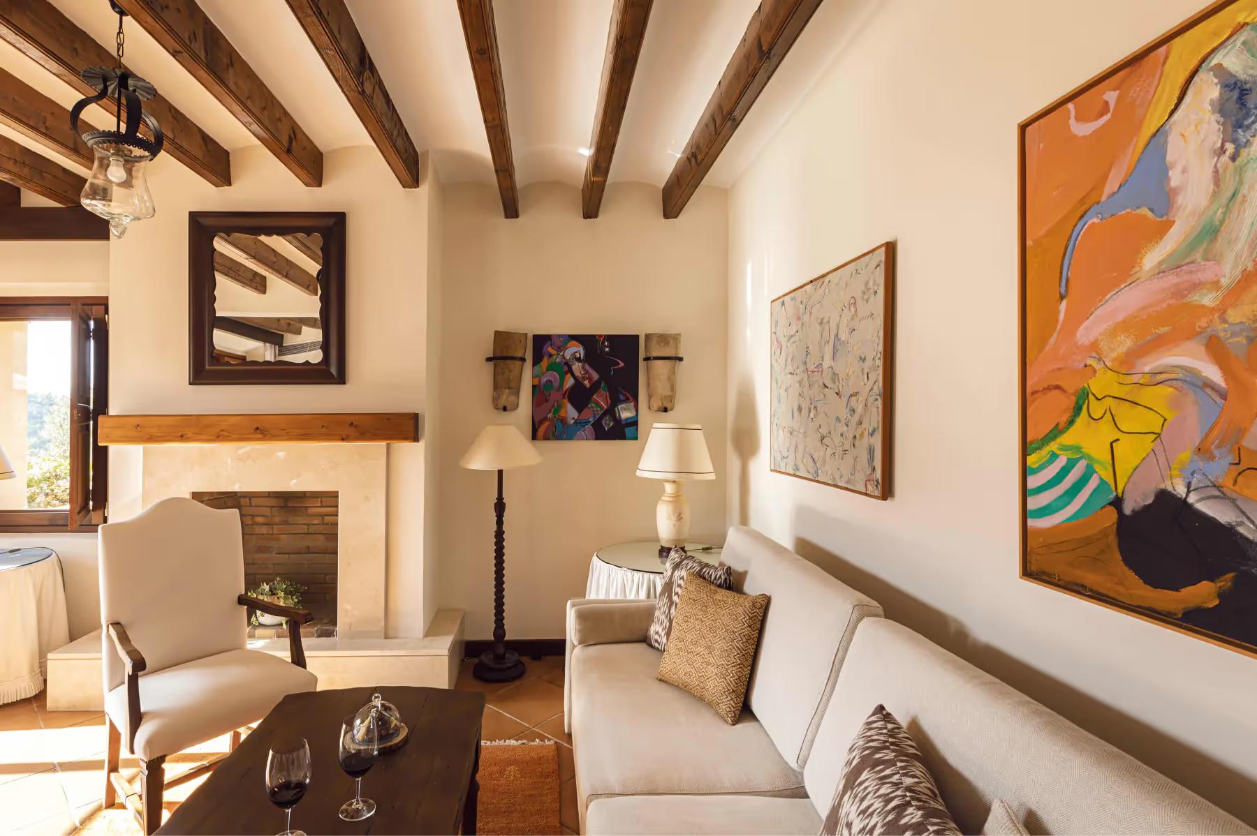 La Residencia: living area with upholstered seating, framed artwork, exposed wooden beams, and stone fireplace