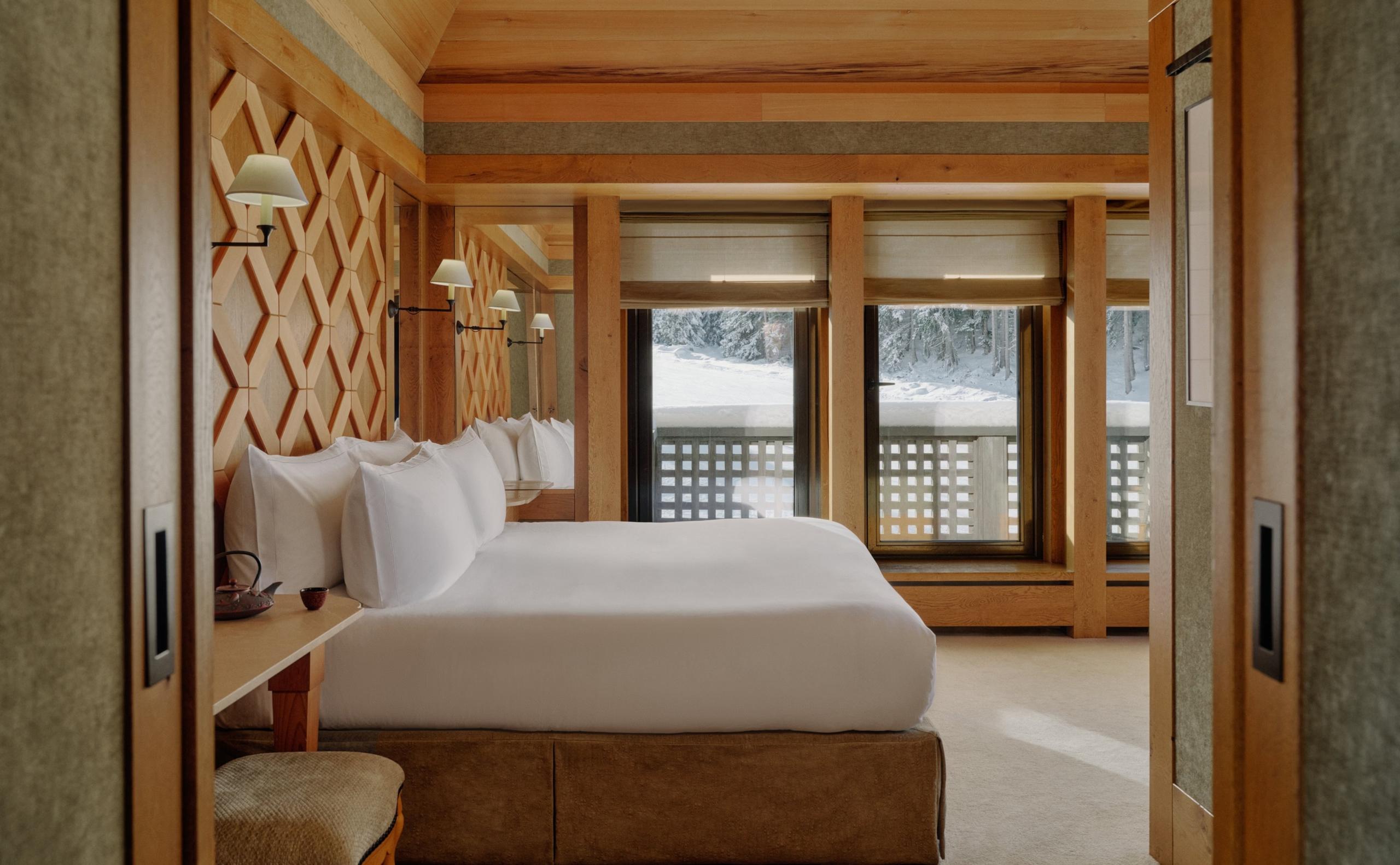 Aman Le Mélézin: bedroom with a diamond lattice wood accent wall and glass doors onto a snowy balcony