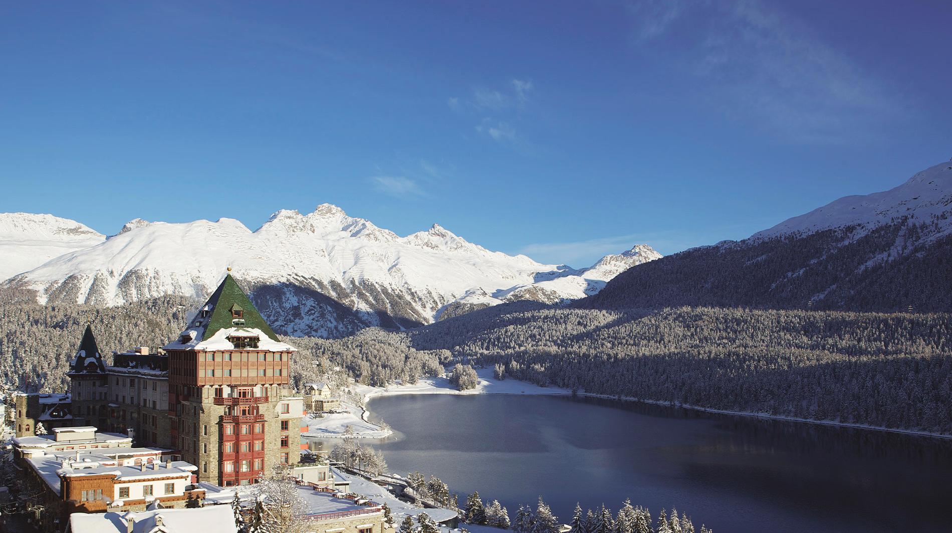 Exterior view of red-brick building on snowy lakeside with pine forest