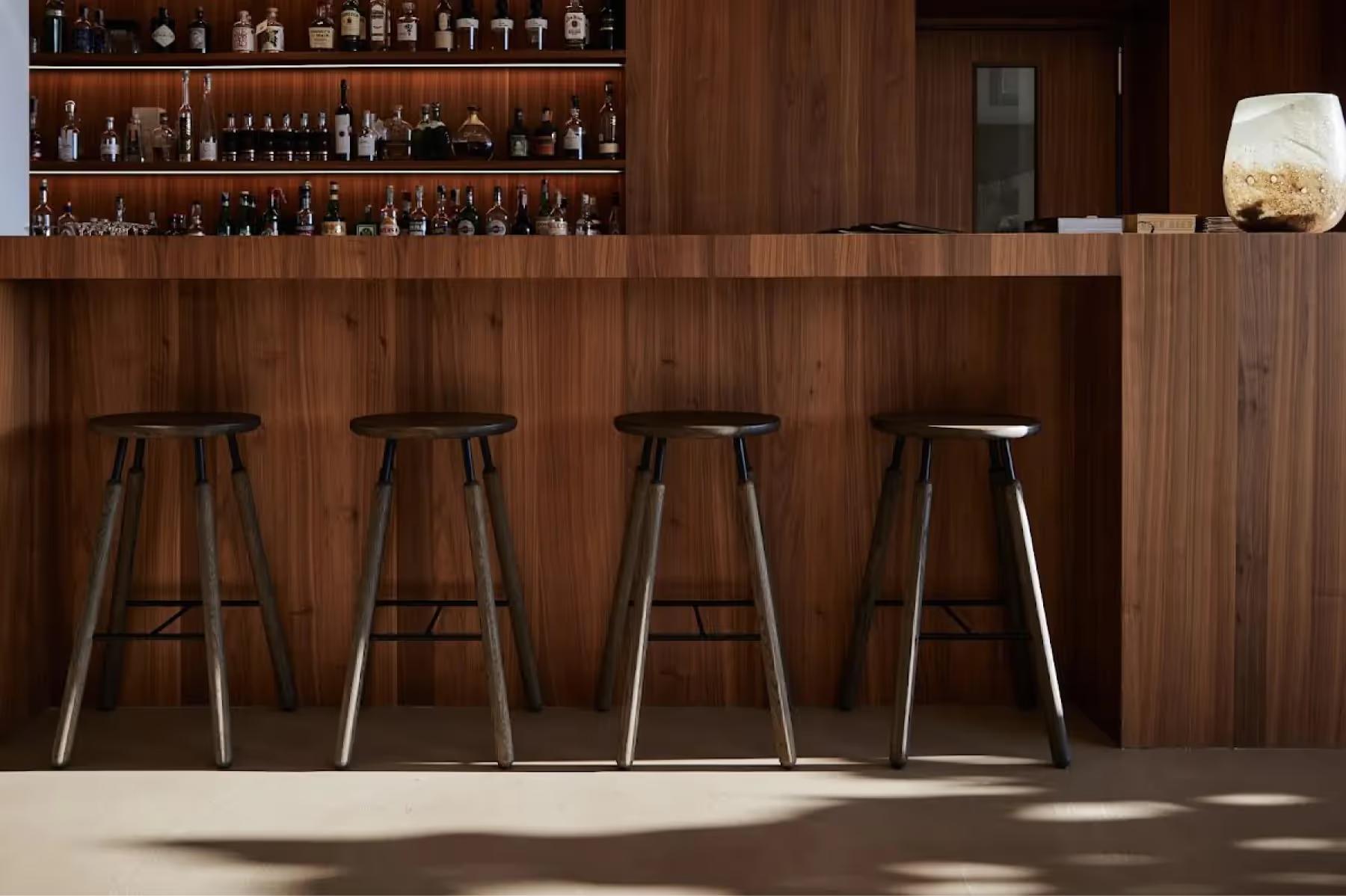 Restaurant bar counter in dark wood with bottled spirits on shelves behind and bar stools