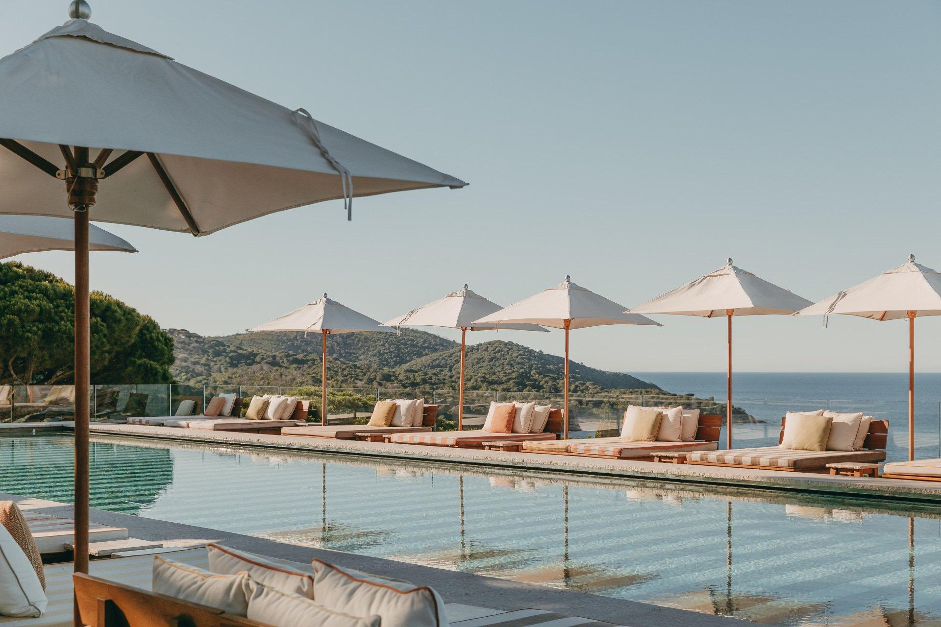 Pool deck with striped umbrellas and lounge chairs facing sea at sunset