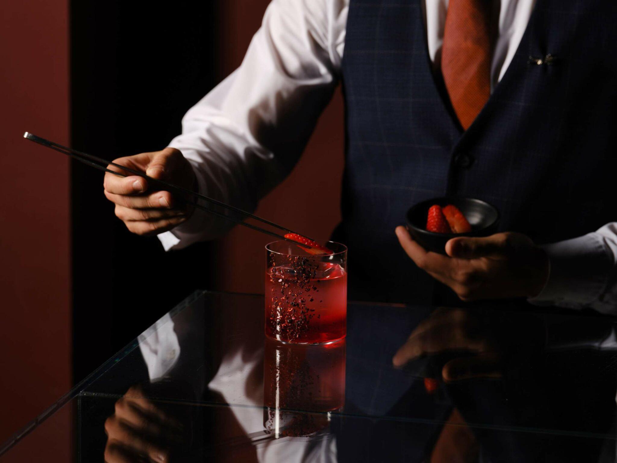 Mandarin Oriental Conservatorium, Amsterdam: bartender in a waistcoat using long tweezers to garnish a red cocktail on a reflective bar