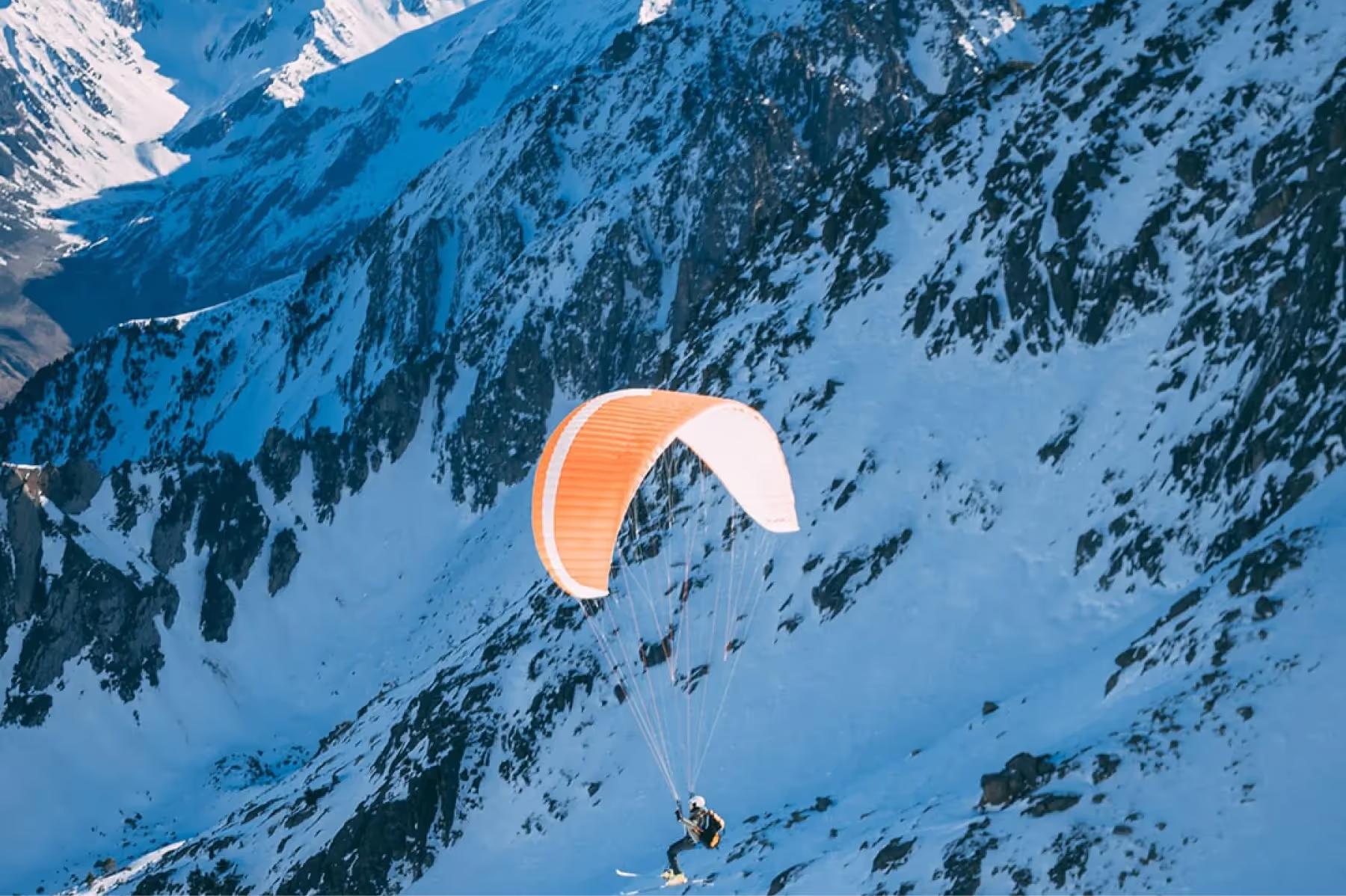 Badrutt’s Palace Hotel: paraglider in orange parachute soaring above snow-covered alpine mountains