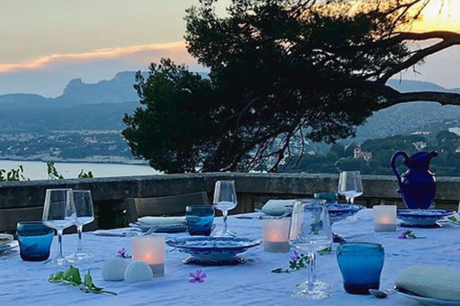Le Domaine de Canaille: outdoor dining setup at dusk overlooking turquoise sea with coastal landscape backdrop