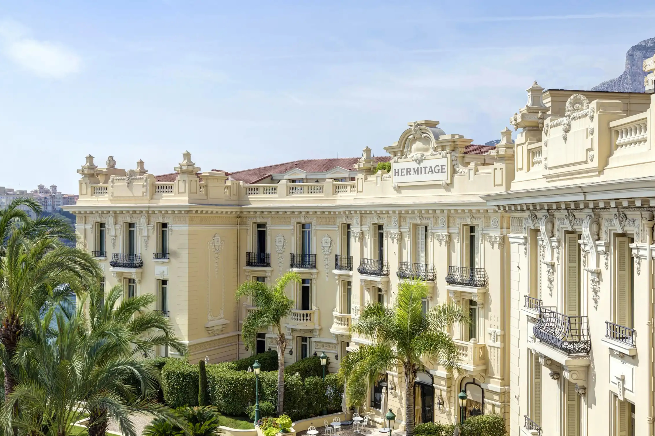 Hôtel Hermitage Monte-Carlo: pale stone façade with arched windows and columned entry, tropical palms visible on square