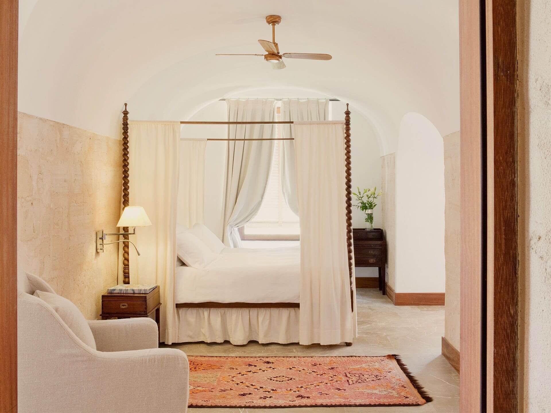 Cap Rocat: a window draped in cream linen overlooks pale grass and turquoise sea at dusk