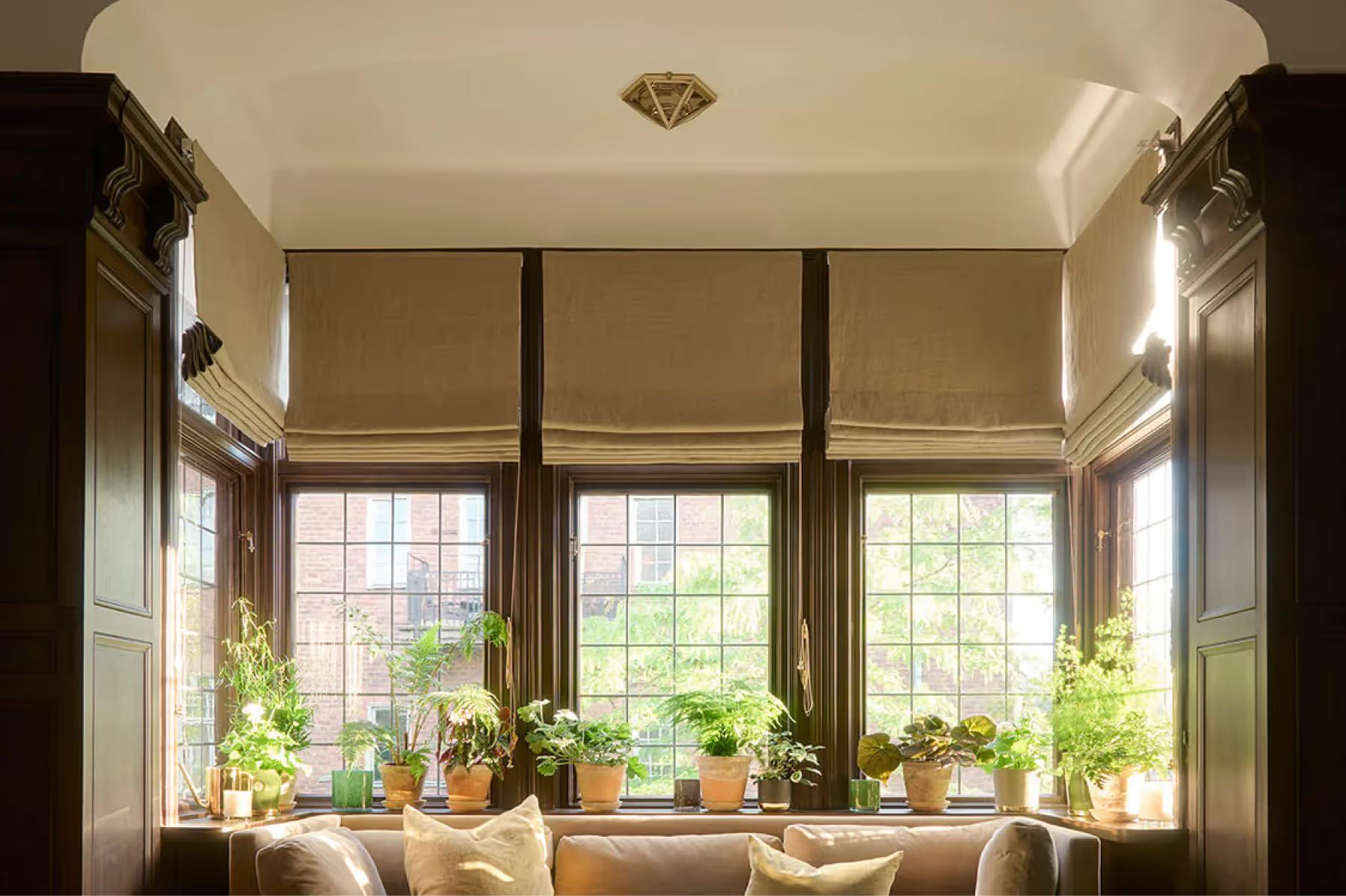 Ett Hem: a window seat with large arched windows, cushions, and potted plants overlooking the exterior