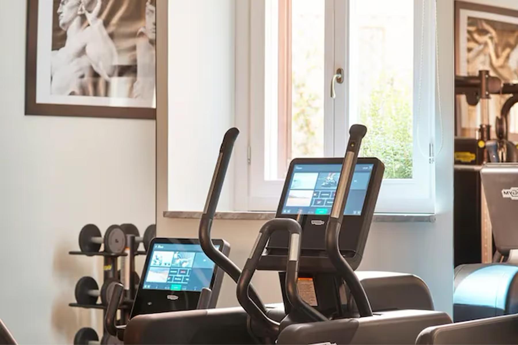 Hotel Eden: a fitness studio with multiple stationary bikes, screens, and windows looking onto an interior courtyard
