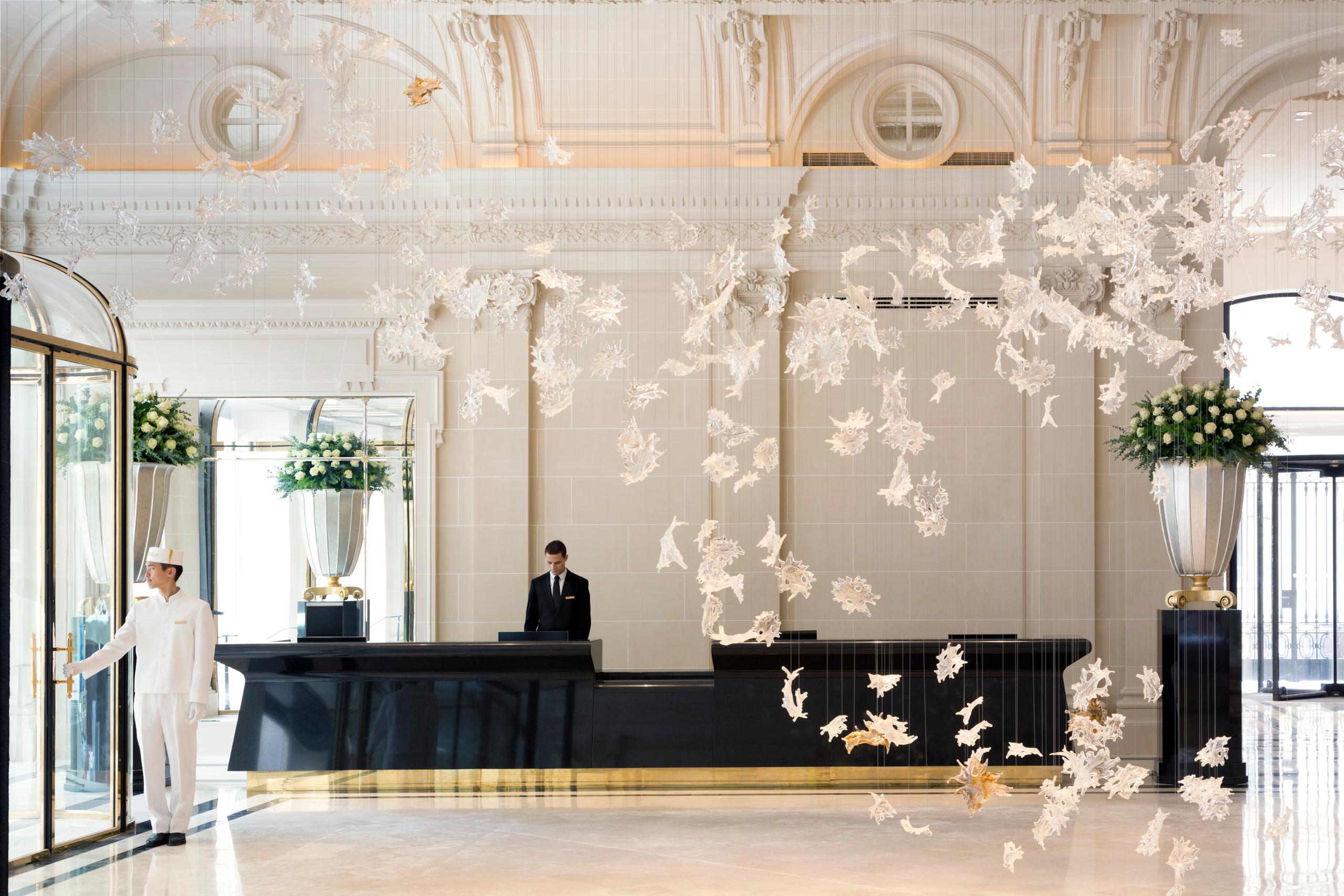 Grand lobby space with cream ceilings, gilded details, hanging installations, and a reception desk