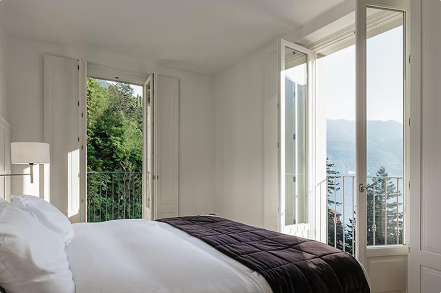 Bright bedroom with white linens and large windows overlooking the lake