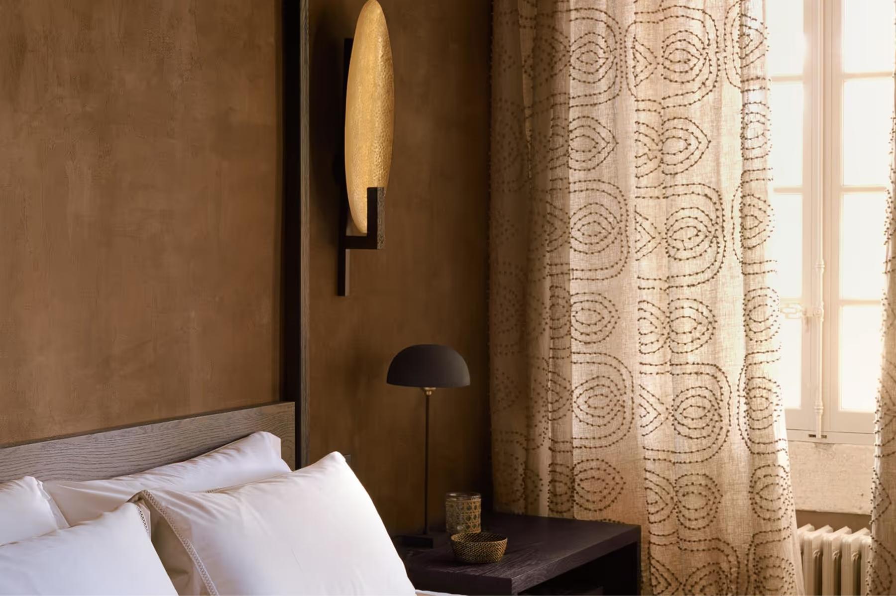 Le Mas de Chabran: bedroom corner with warm tan walls, gold patterned curtains, and light wood nightstand